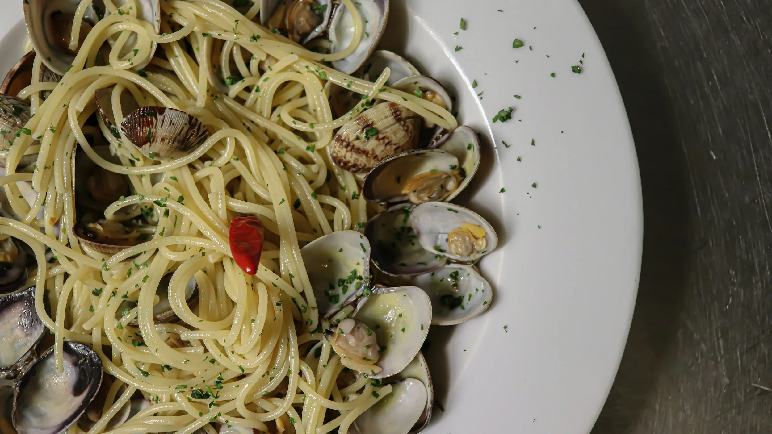 A plate of spaghetti with clams, garnished with chopped parsley and a red chili pepper.