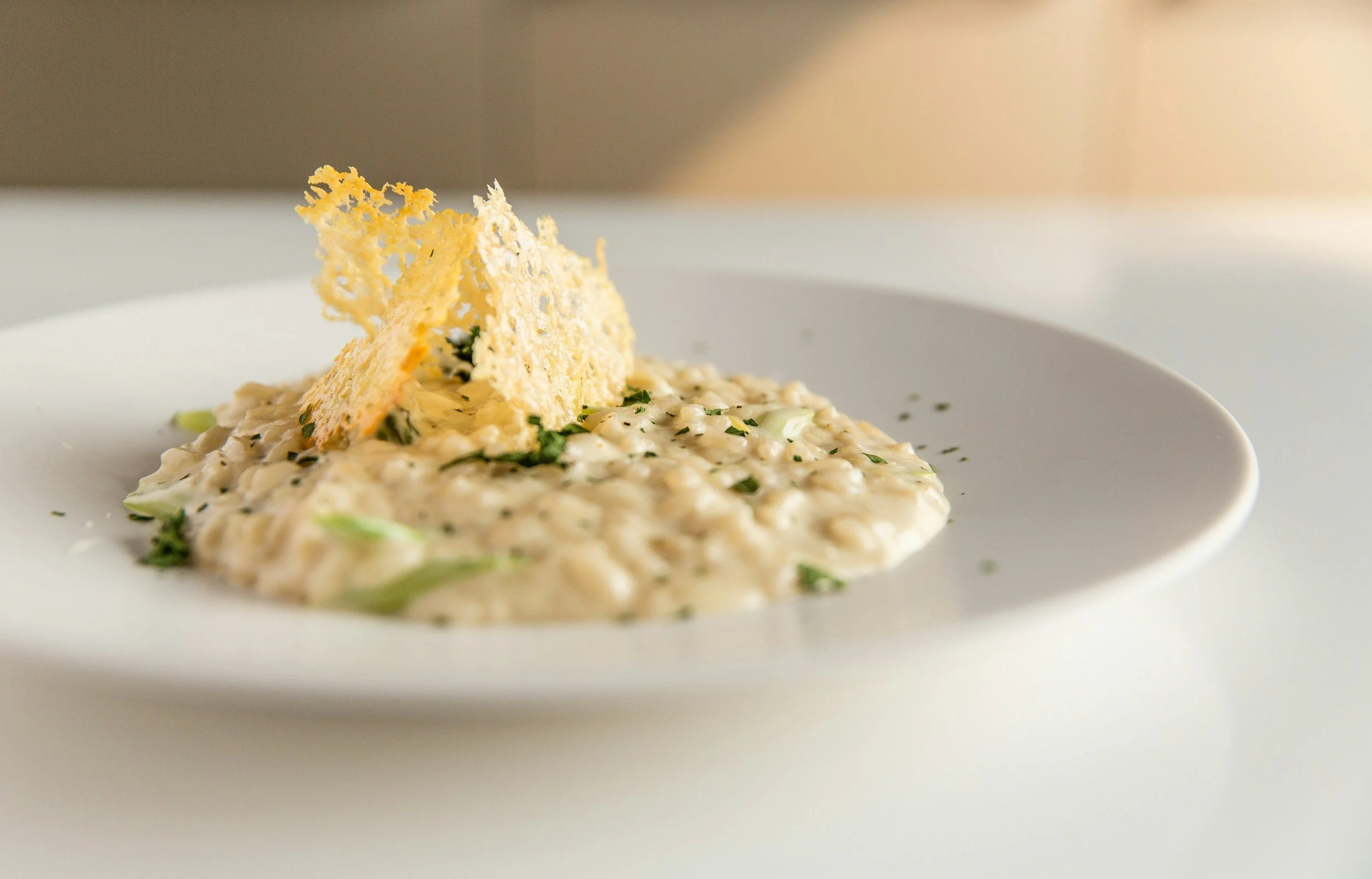 Creamy risotto topped with crispy parmesan cracker on a white plate