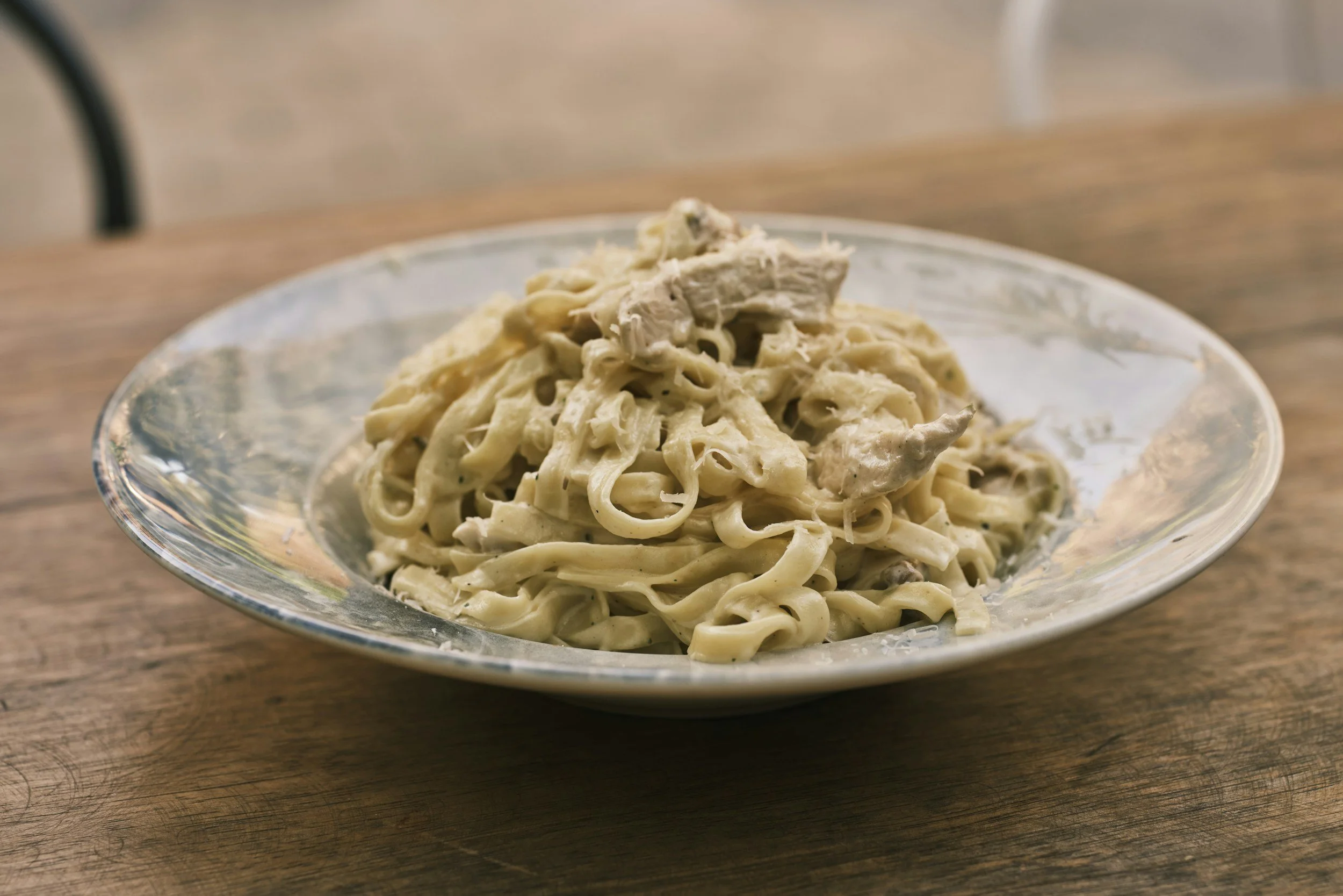 Plate of fettuccine pasta with creamy Alfredo sauce and shredded chicken on top.