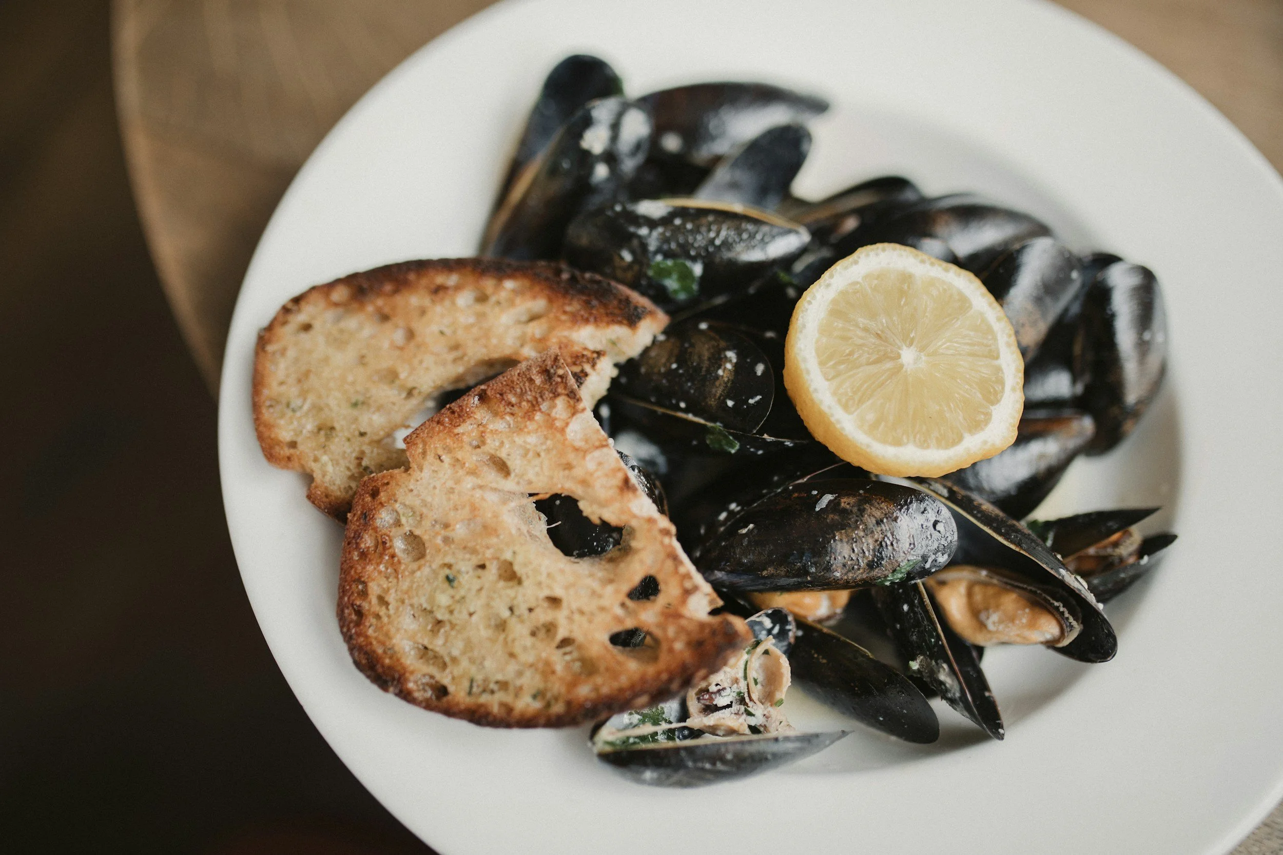 A white plate of mussels with half a lemon and two slices of toasted bread.