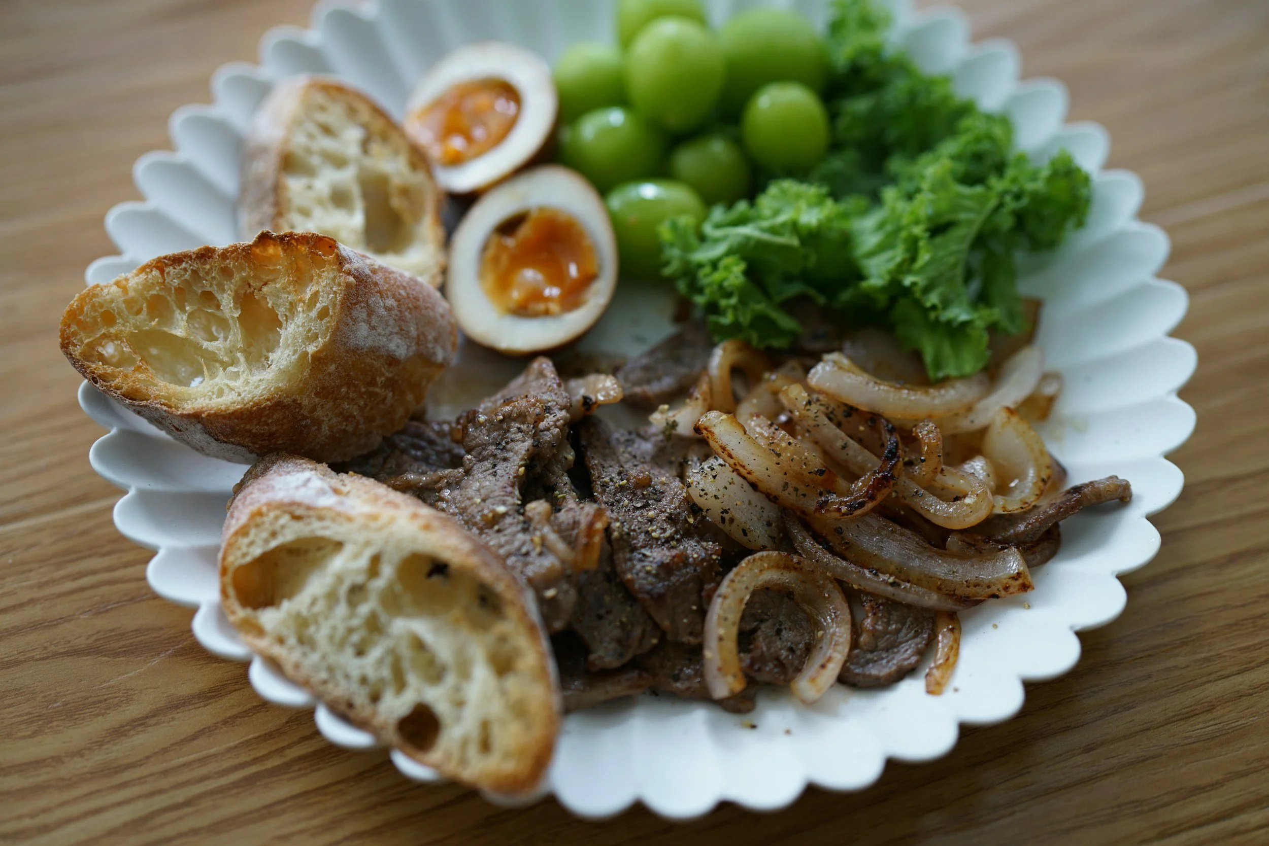 A plate of food with sautéed onions and beef, boiled eggs, green peas, leafy lettuce, and pieces of toasted bread on a wooden table.
