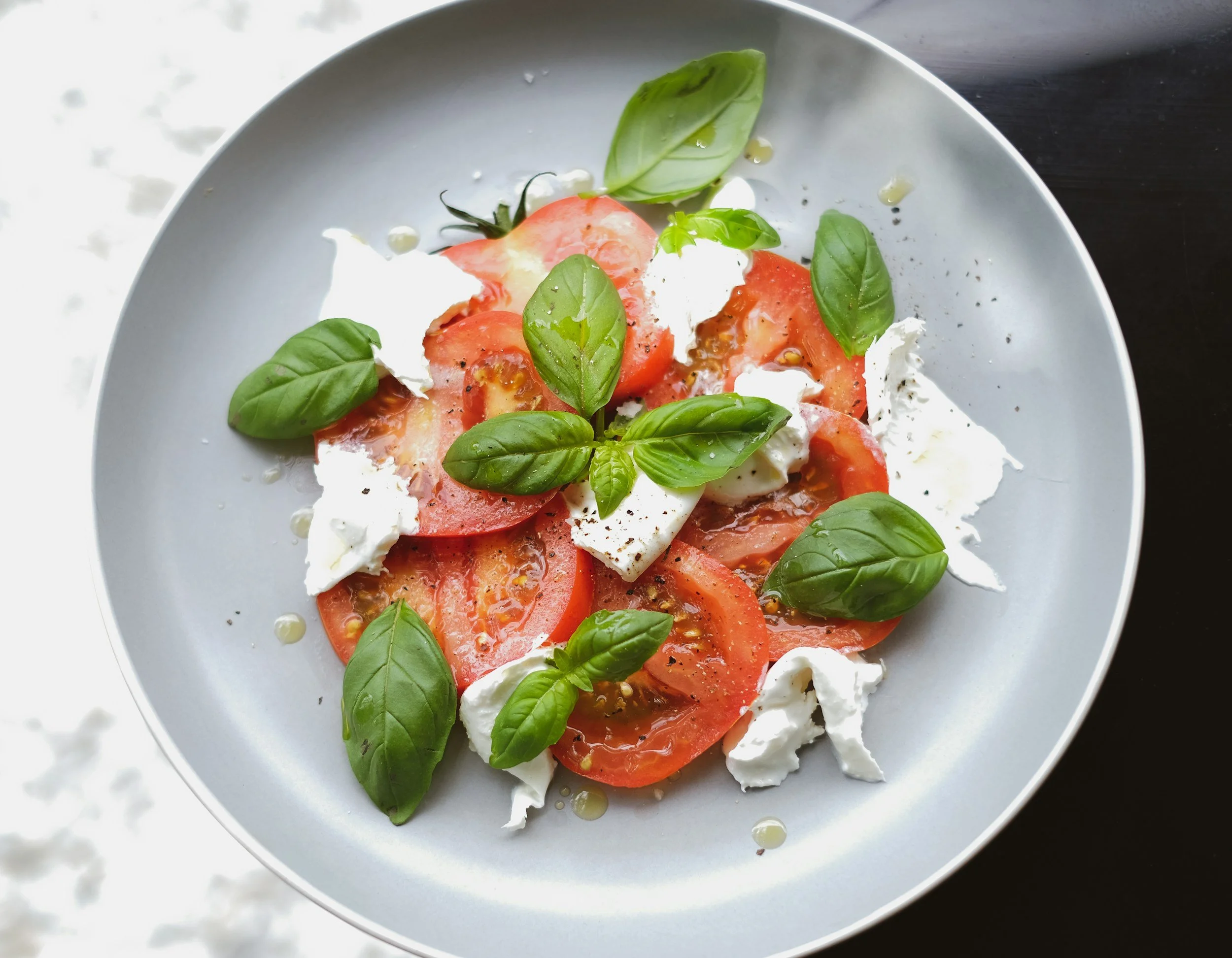 A plate of sliced tomatoes, fresh basil leaves, mozzarella cheese, and olive oil drizzled on top.
