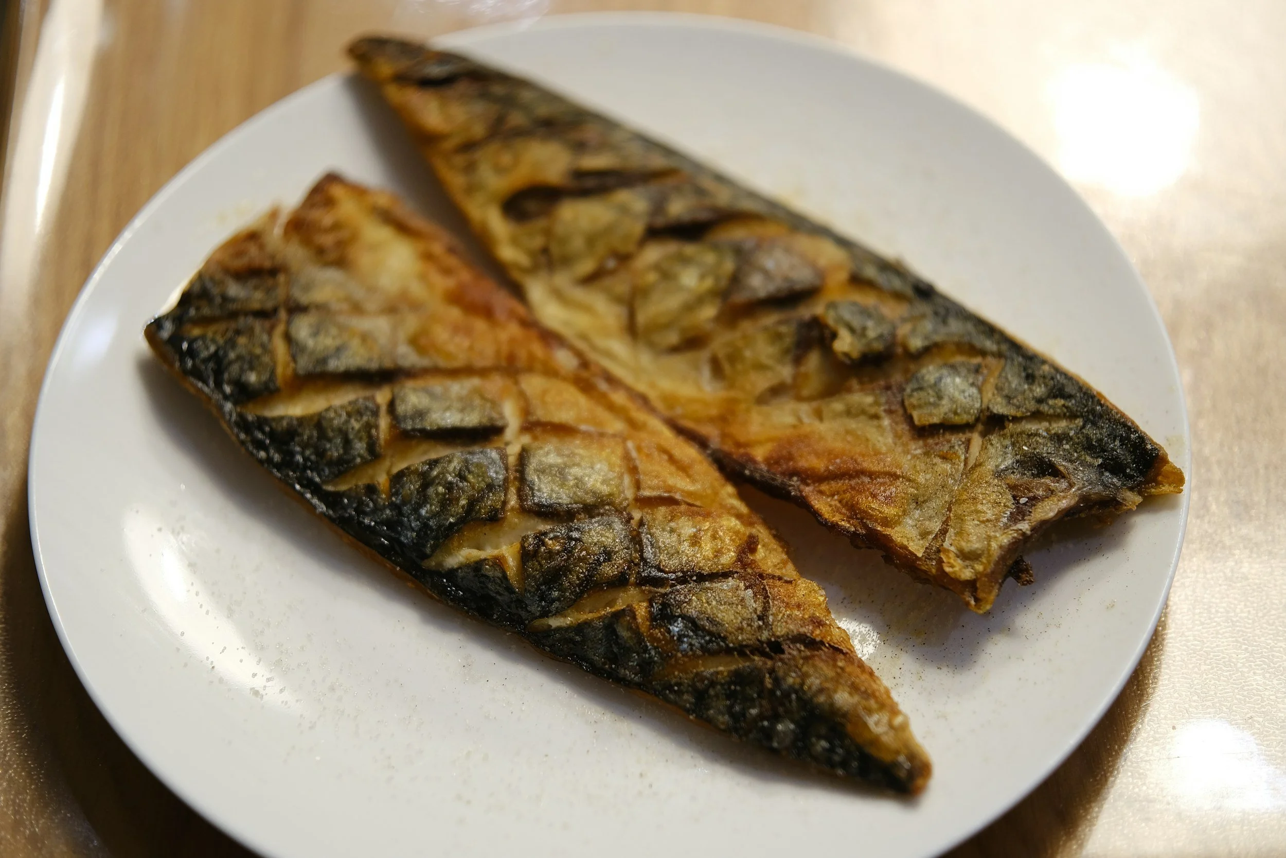Two grilled fish fillets on a white plate, showing charred skin and golden flesh.