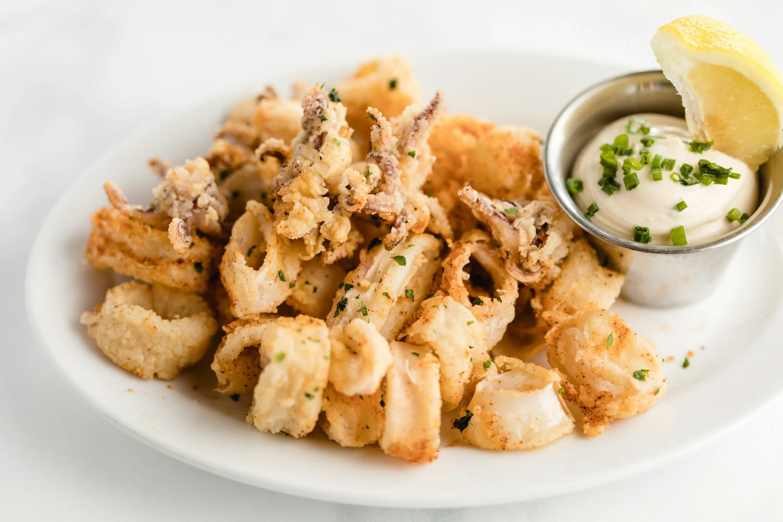 Fried calamari with a side of creamy dipping sauce garnished with chopped chives and a lemon wedge