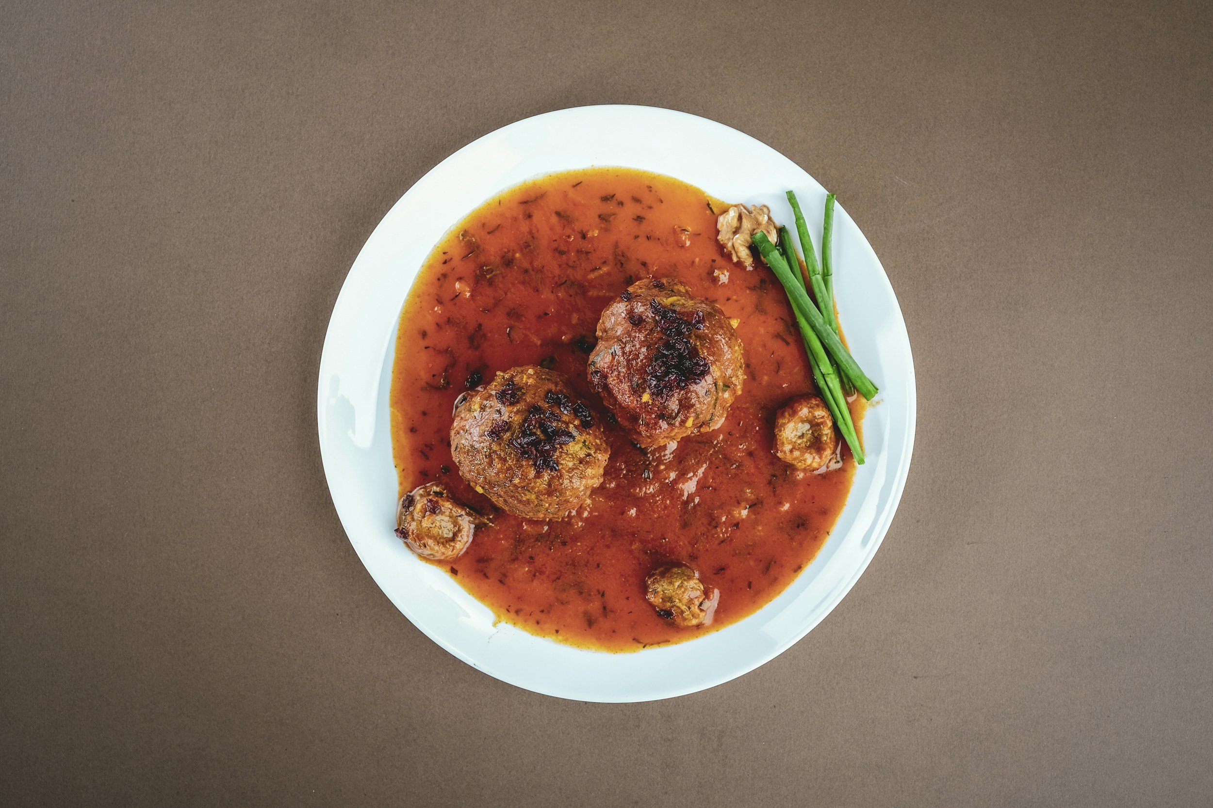 Plate with two meatballs in tomato sauce, garnished with green onions.