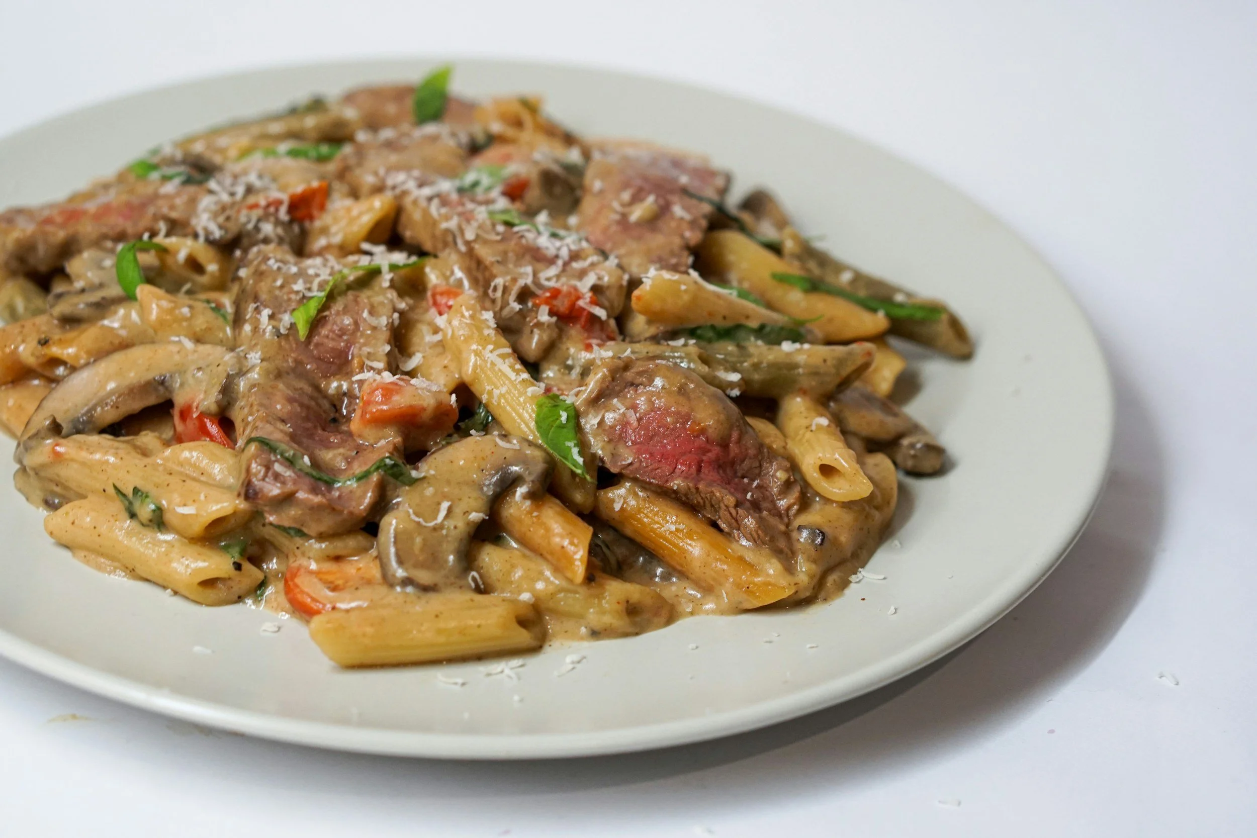 Plate of creamy beef stroganoff with penne pasta, mushrooms, beef, and vegetables