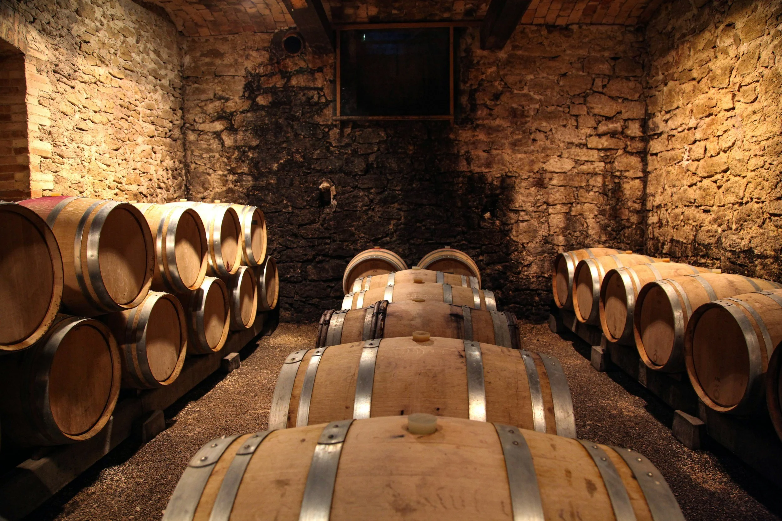 Wine barrels stored in a cellar with stone walls and wooden beams.