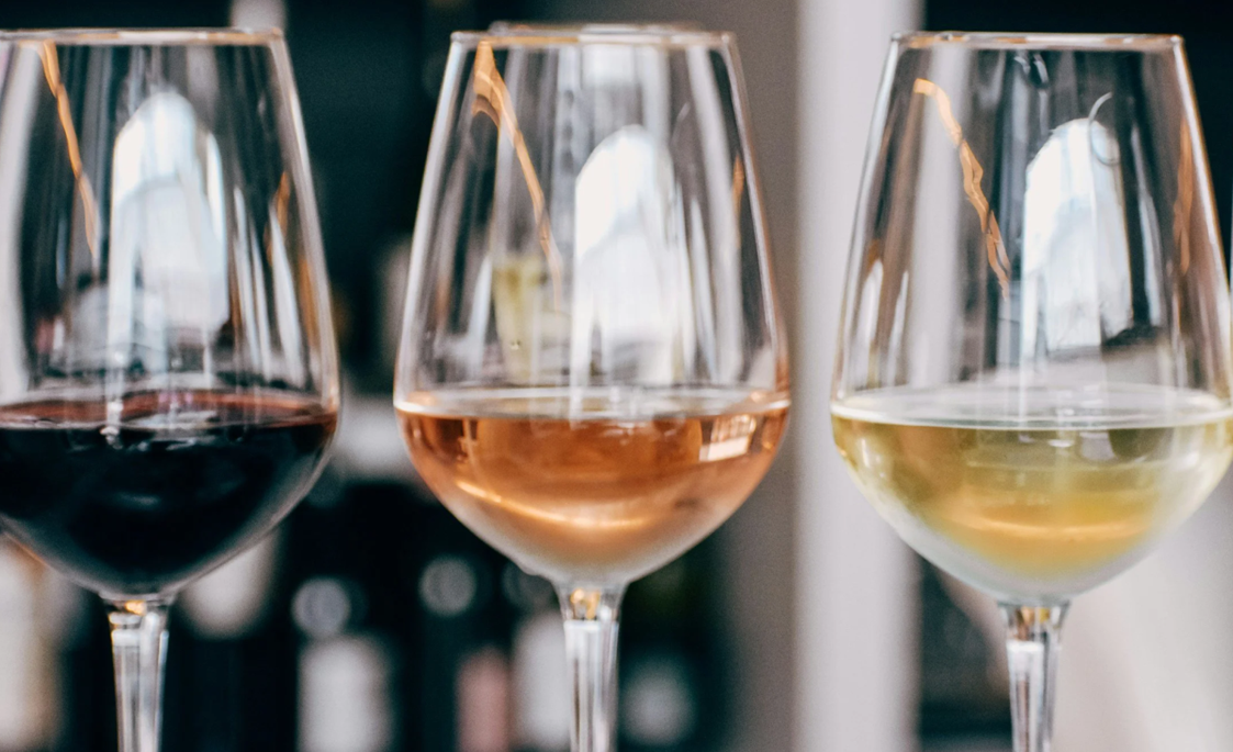 Three wine glasses with red, rosé, and white wine on a bar or table.
