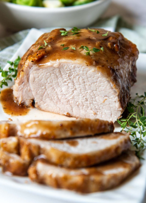 Sliced cooked chicken breast with gravy and fresh herbs, served on a white platter.