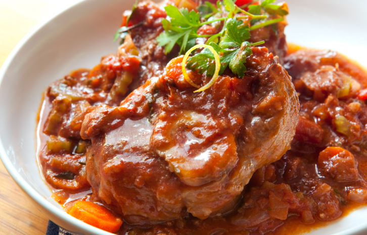 Beef pot roast with vegetables in a tomato-based sauce, garnished with cilantro and sliced green onions on a white plate.