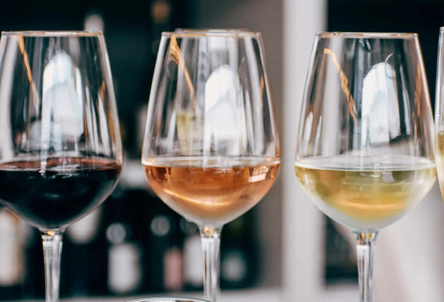 Close-up of three wine glasses filled with red, rosé, and white wine, set against a blurred background.