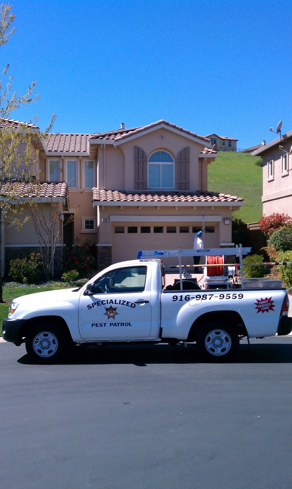 White pest control truck with the words 'Specialized Pest Patrol' parked on a residential street in front of a two-story house with a tile roof and green lawn.