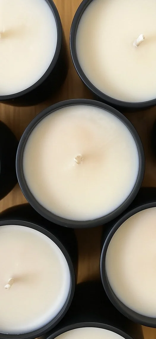 Close-up of several white candles in black containers on a wooden surface.