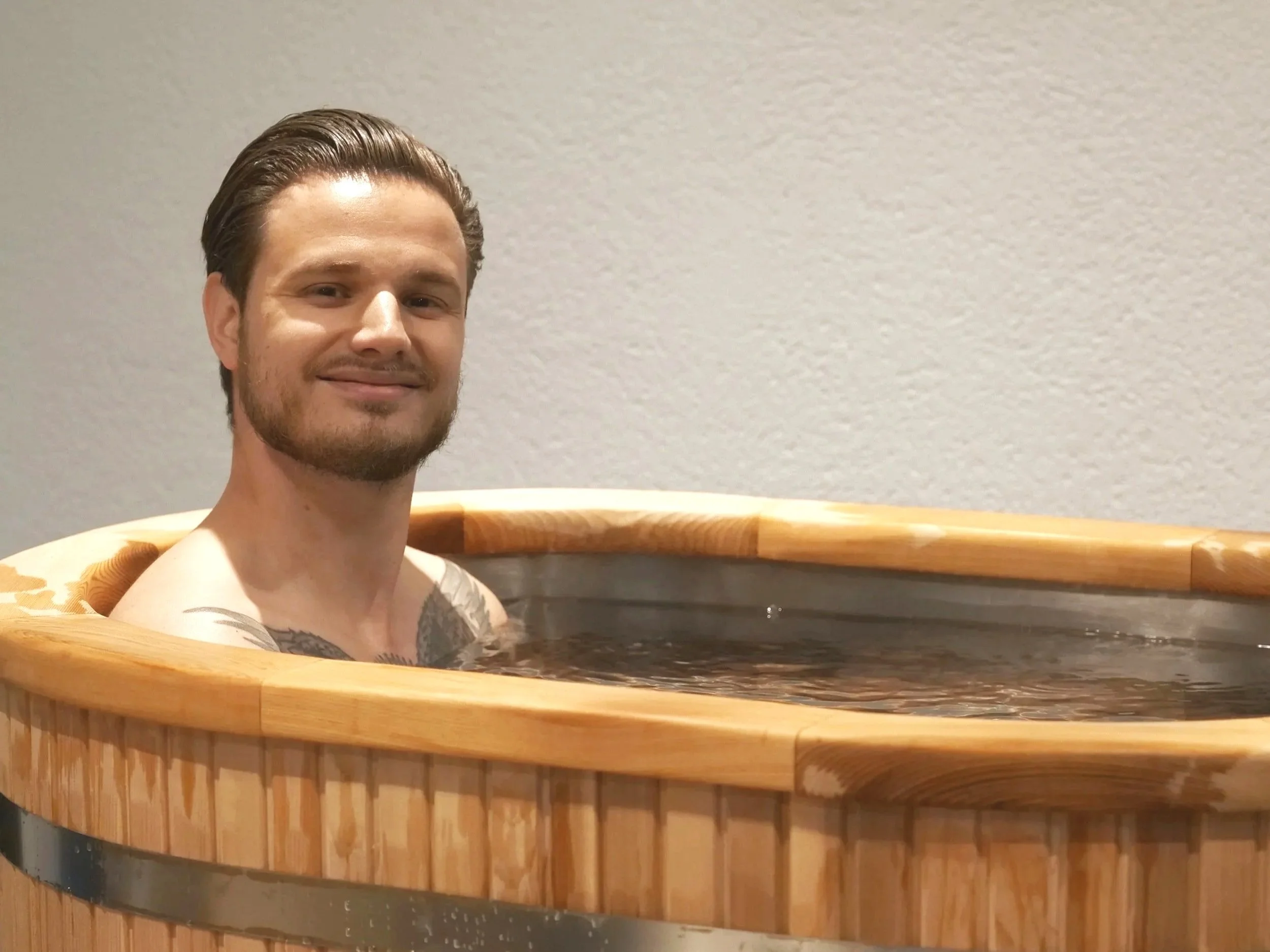 Deux baignoires en bois avec deux petites escaliers en bois devant, sur un fond de mur blanc avec l'inscription "Mettre du confort dans l'inconfort" en lettres noires.