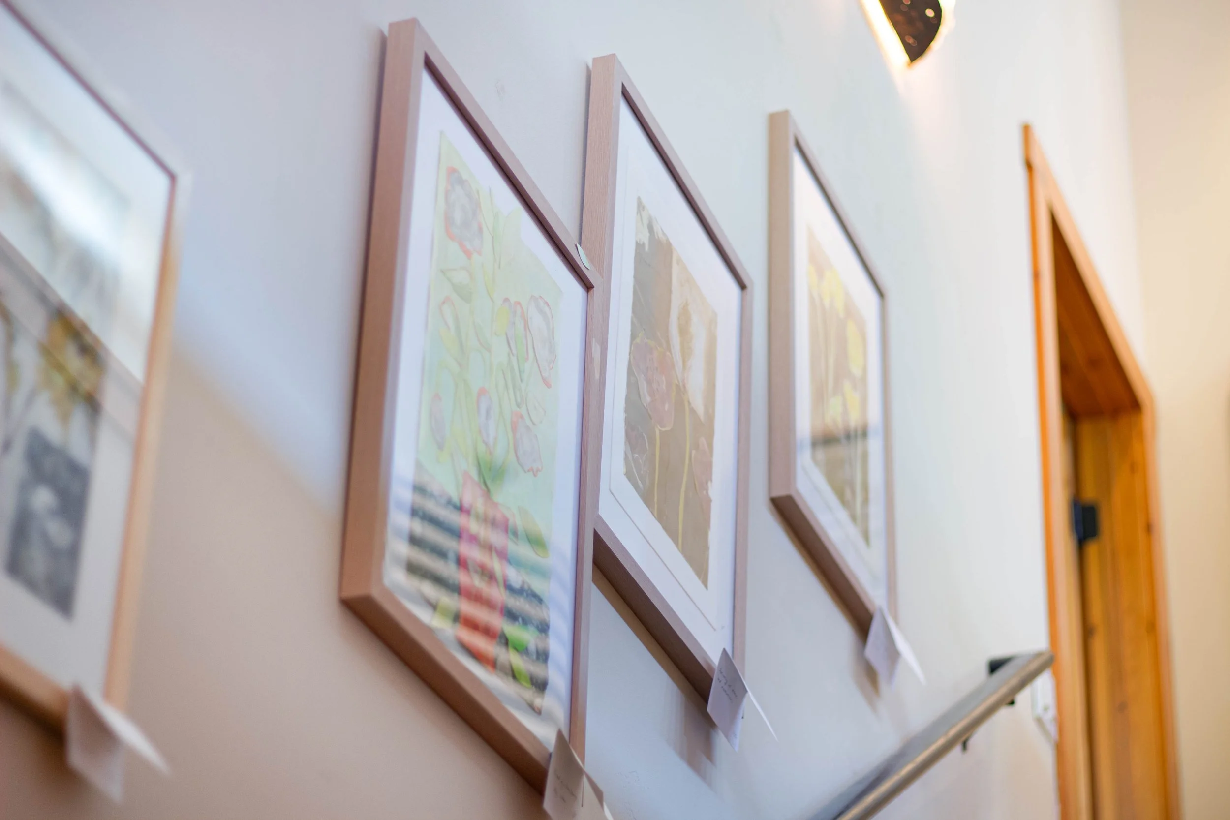 A series of framed artwork hanging on a wall, featuring floral illustrations, in a gallery setting.