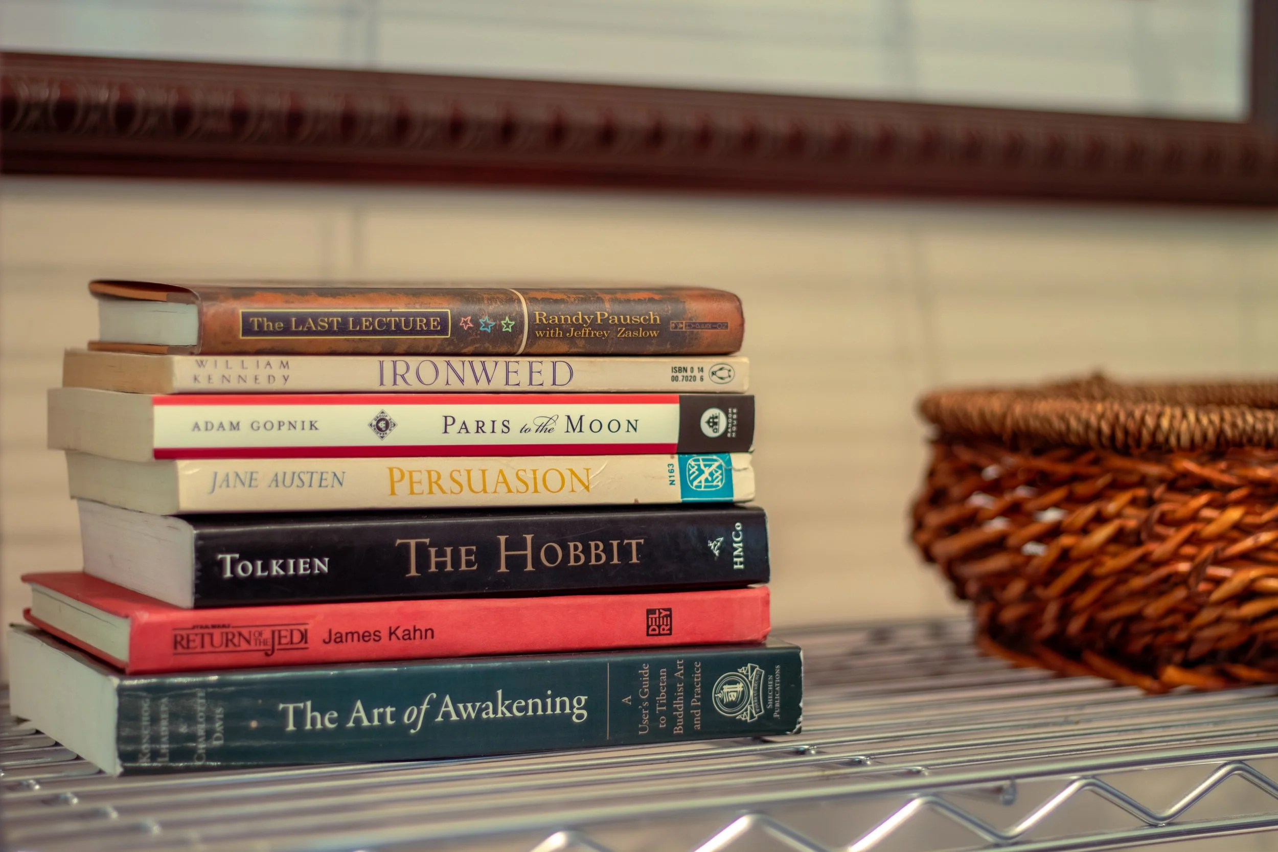 Stack of books on a metal shelf with a woven basket to the right