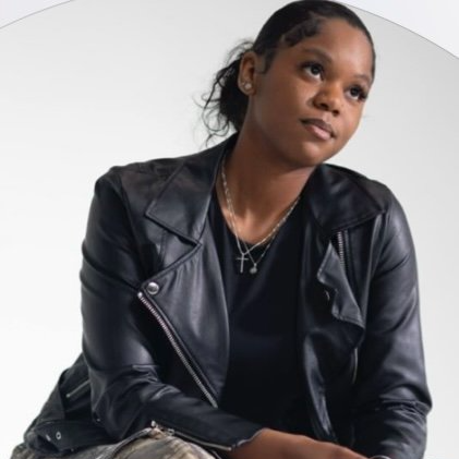 Portrait of a woman wearing a black leather jacket and layered necklaces, looking thoughtfully to the side against a white background.