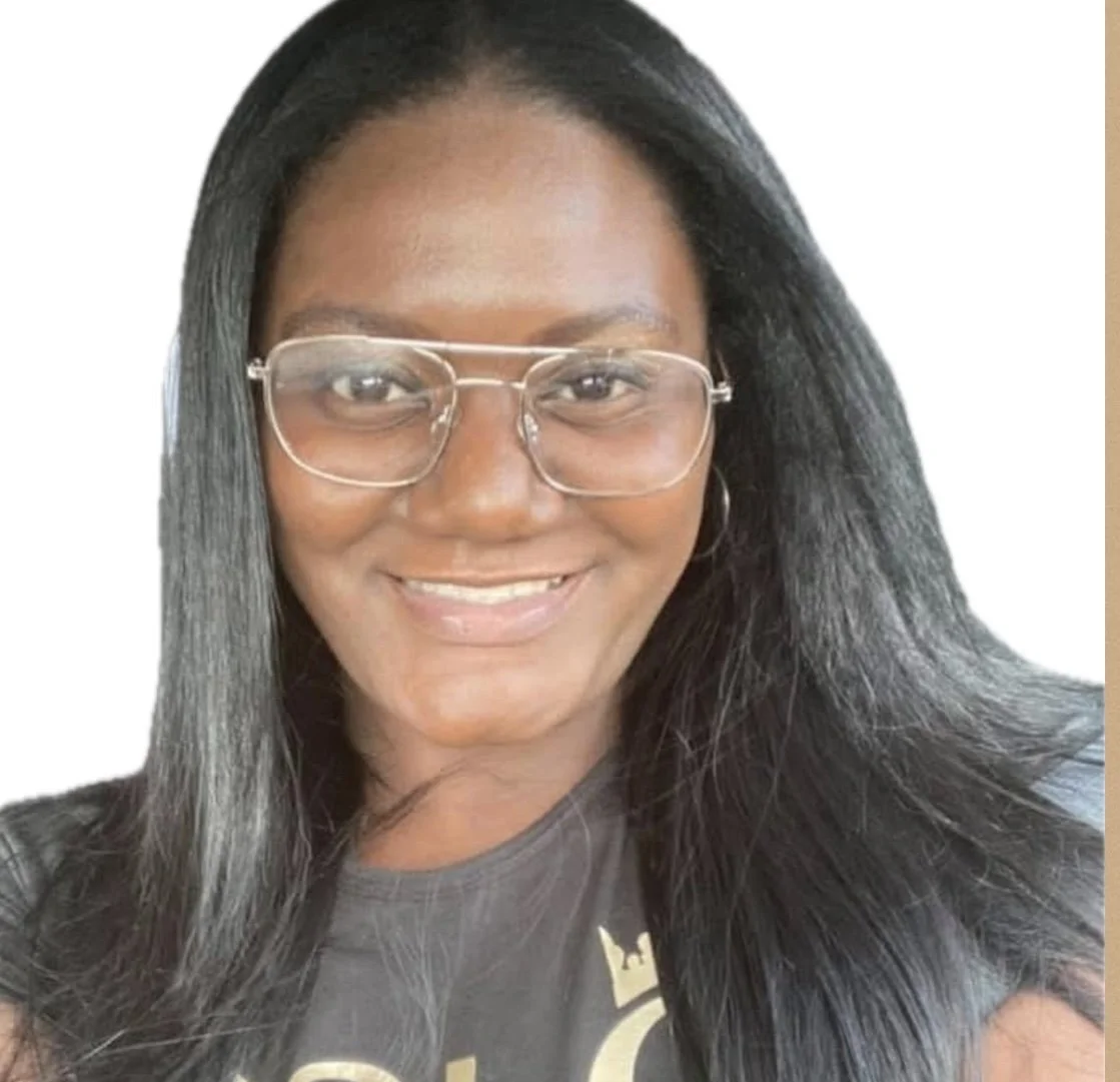 A smiling woman with long black hair and glasses, wearing a dark T-shirt with a gold design, against a plain white background.