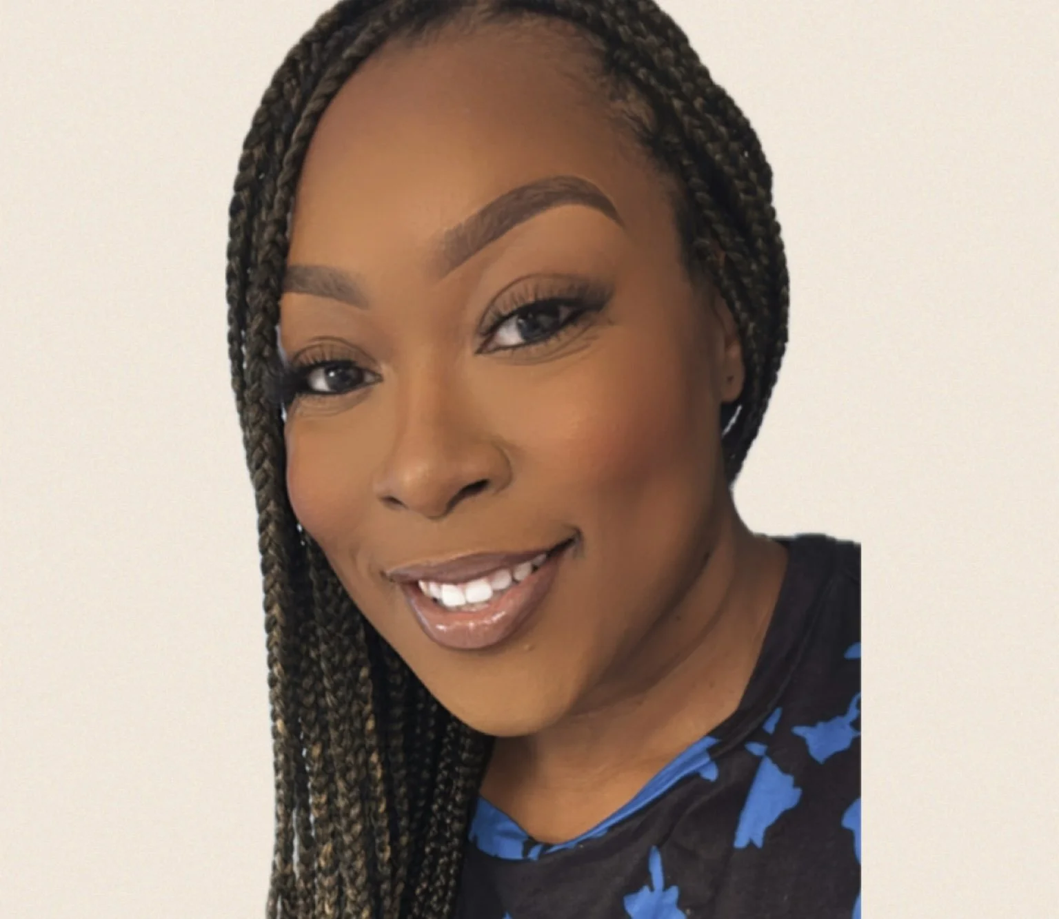 Close-up of a woman with braided hair smiling, wearing makeup and a black shirt with blue accents.
