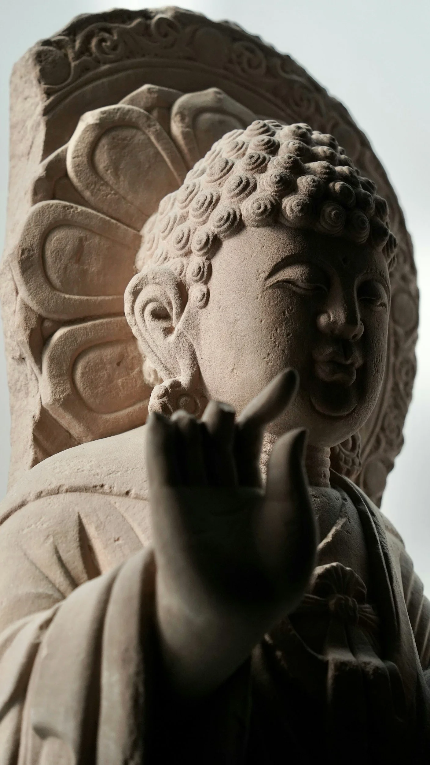Close-up of a stone Buddha statue showing its head, face, and one hand with fingers in a mudra gesture.