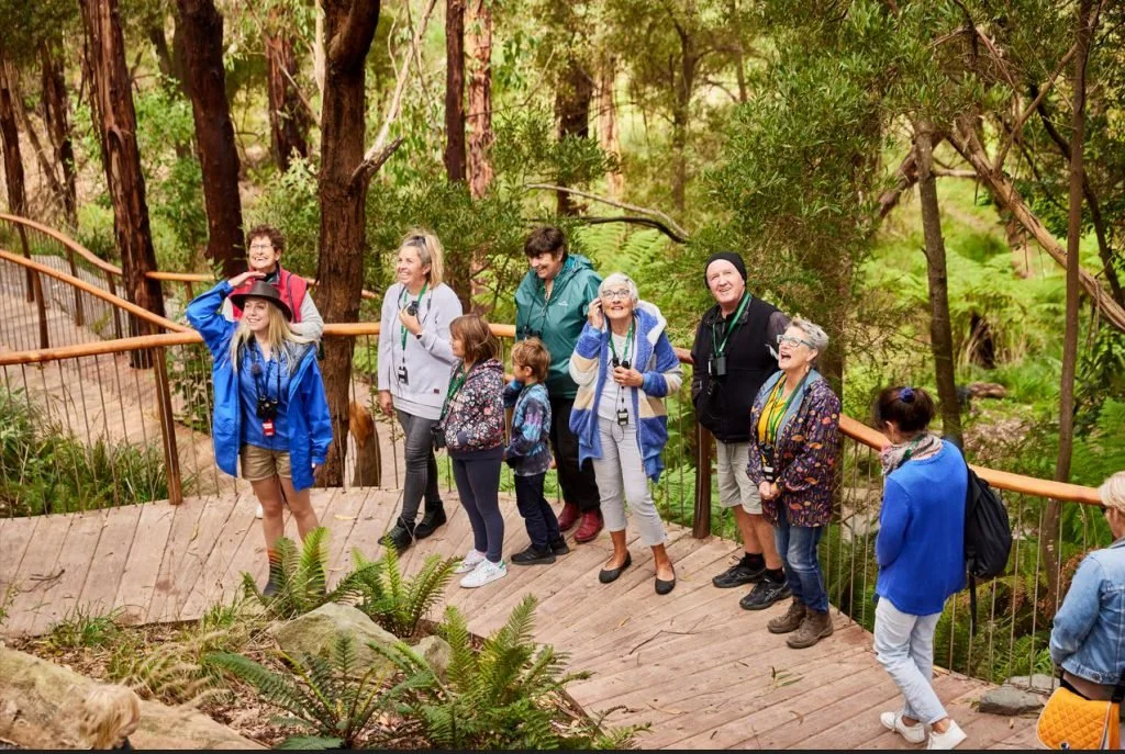 A group of people, including children and adults, standing on a wooden platform in the Wildlife Wonders' sanctuary, smiling and posing for a photo.