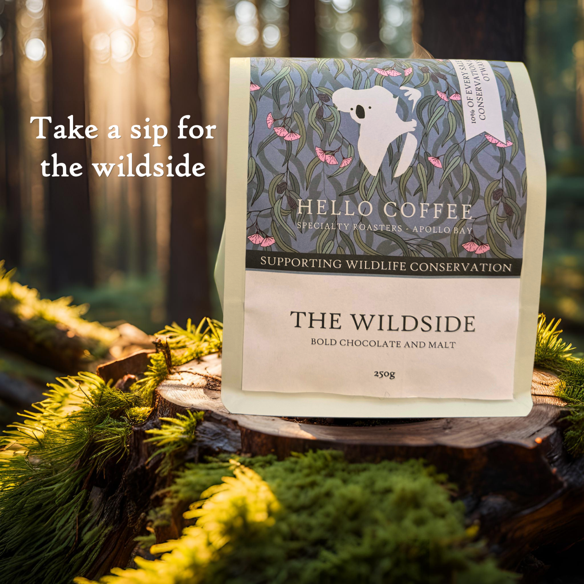 Coffee packet labeled 'The Wildside' with wildlife conservation support message, set outdoors on a moss-covered log surrounded by trees, with sunlight filtering through the forest.