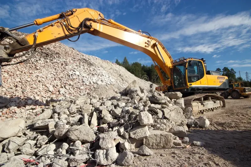 Excavator breaking out and piling concrete rubble during a concrete removal job