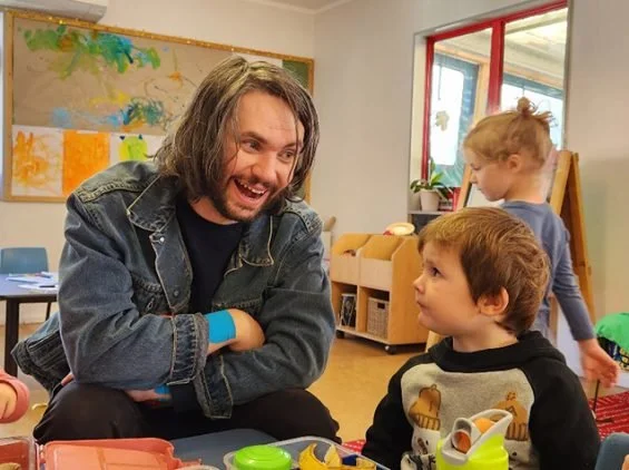 Man laughing and talking with two children in a classroom setting.