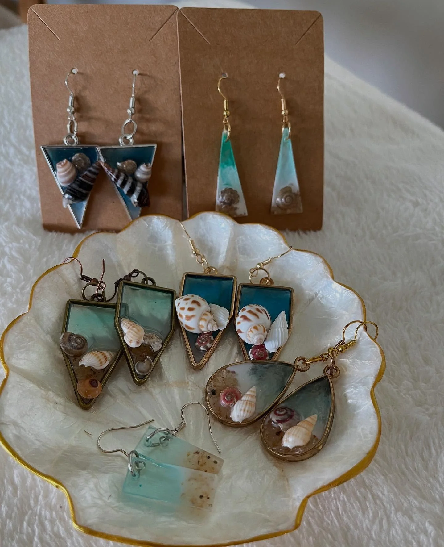 Shelley 

Inspired by rolling waves and coastal calm, these earrings feature fluid swirls of blue and white with delicate seashells embedded within. A graceful ode to the ocean&rsquo;s rhythm.

Assorted bezel shapes available -Pentagon, Triangle, Tea