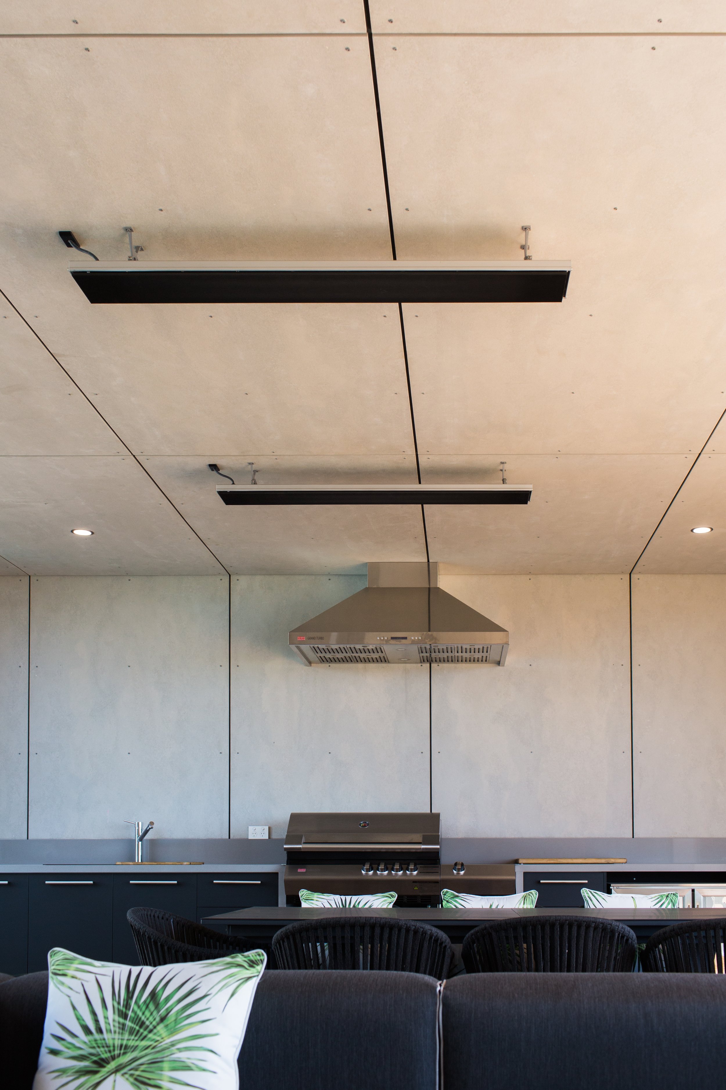 Modern indoor kitchen with black countertops, a stainless steel grill, a range hood, black chairs, and decorative pillows with green leaf patterns.