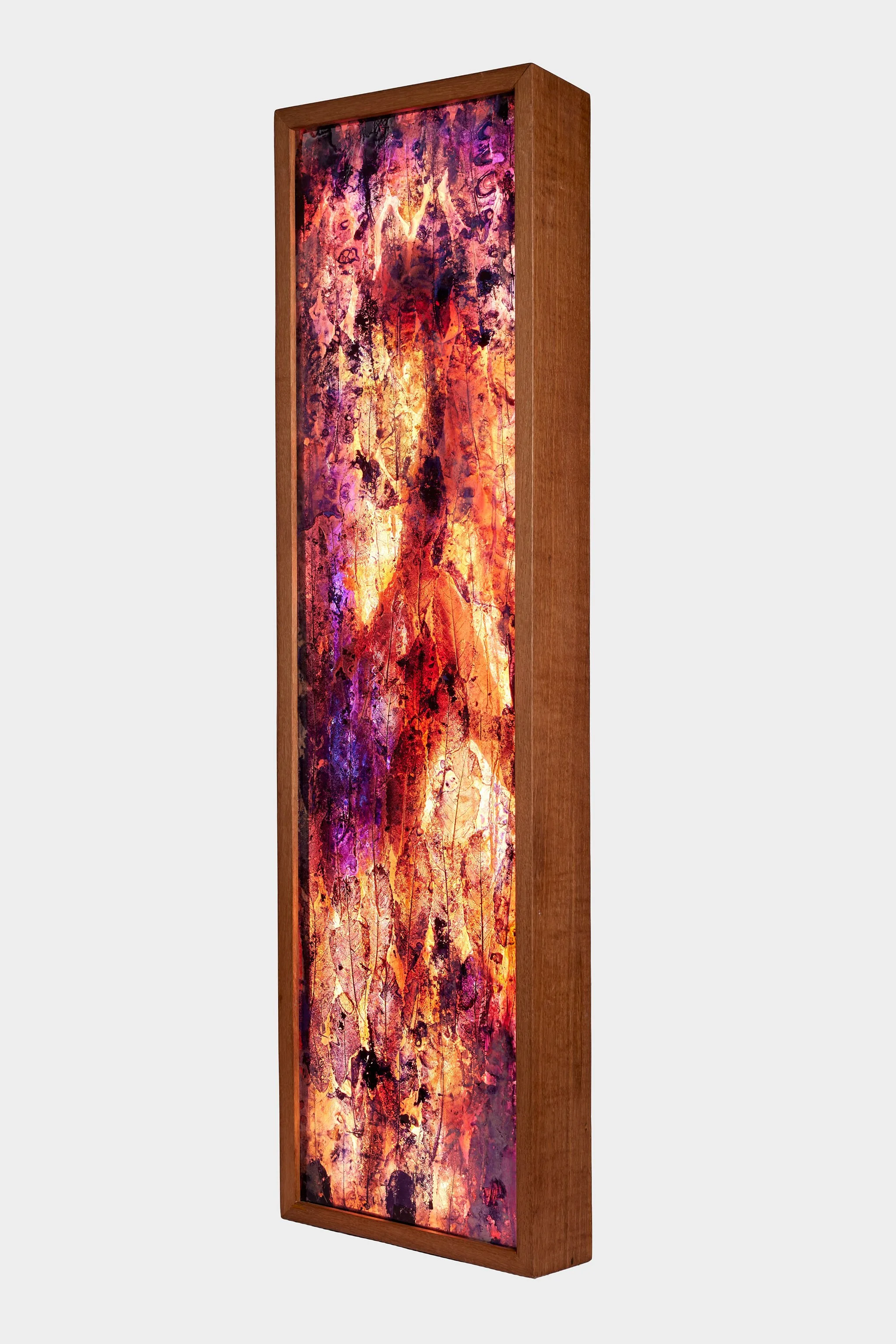 Resined mahoe leaves framed in a tall rectangular light with a female figure with warm colors of orange, red, purple, and black.