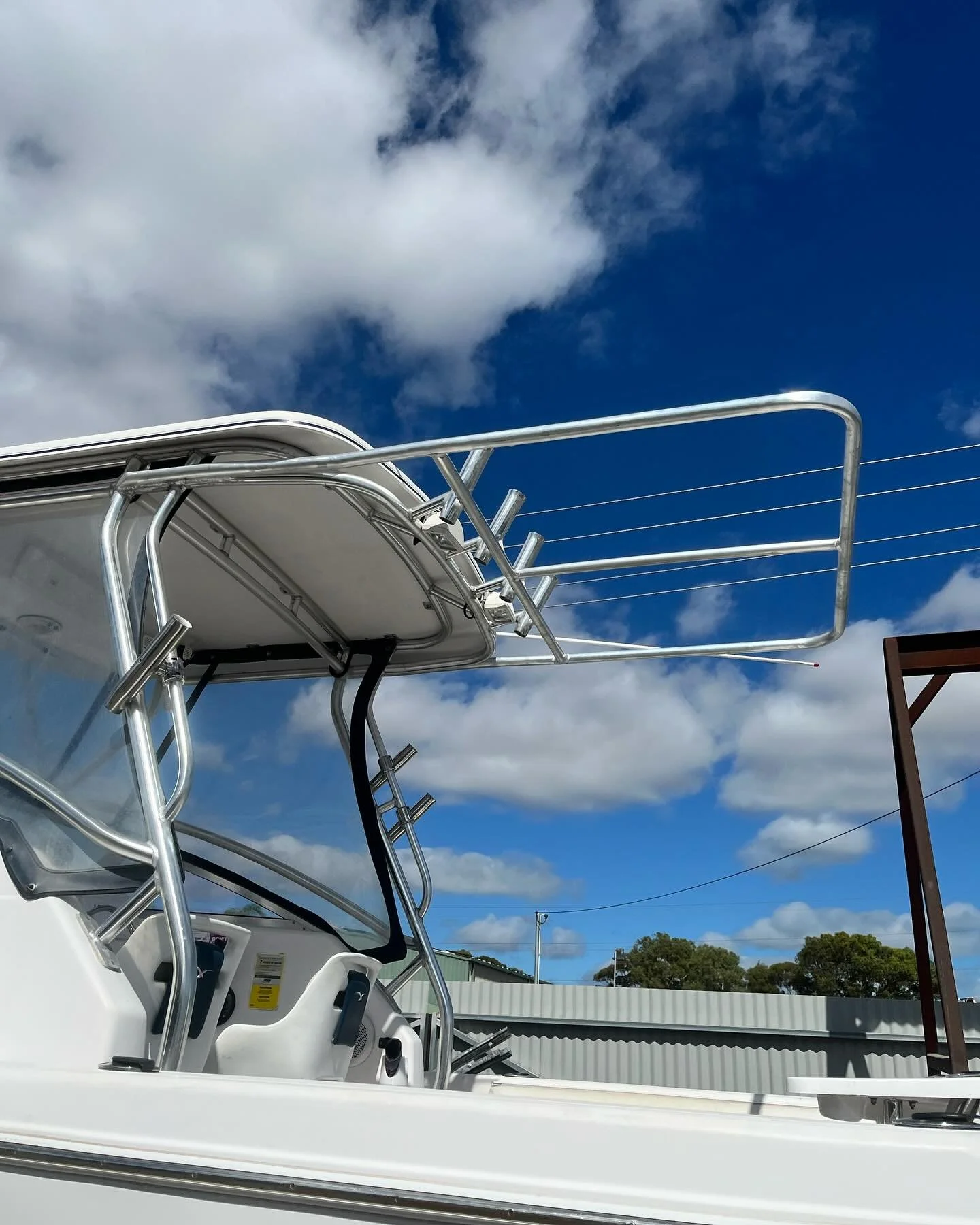 Close-up of a white boat's upper structure with metal railings and antennas against a partly cloudy sky.