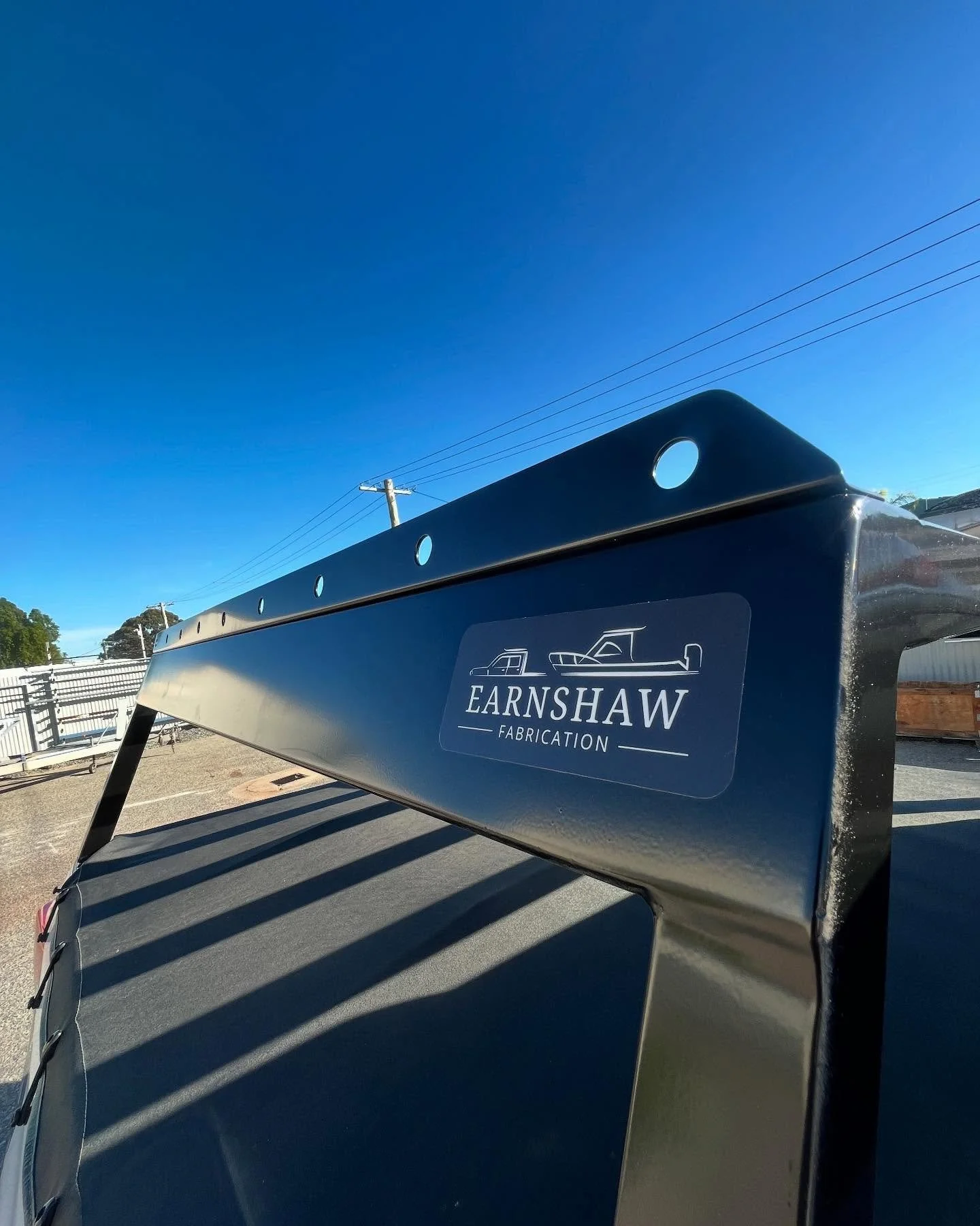 Close-up of a metal boat canopy with the Earshawm Fabrication logo, featuring boat illustrations, under a clear blue sky.