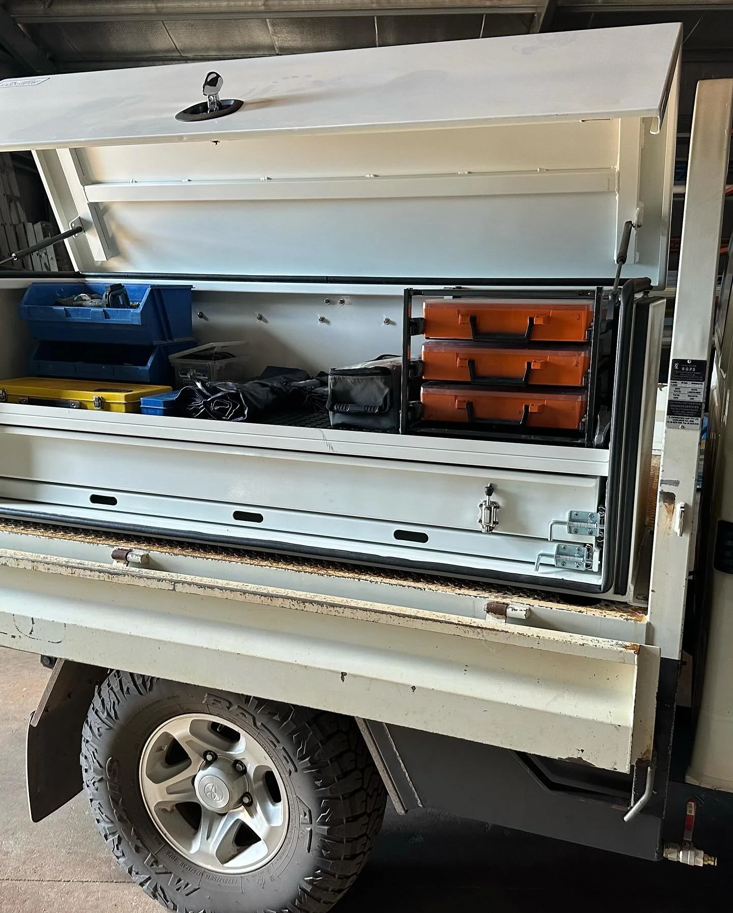 Open utility truck with shelves and storage bins, tools, and equipment inside.
