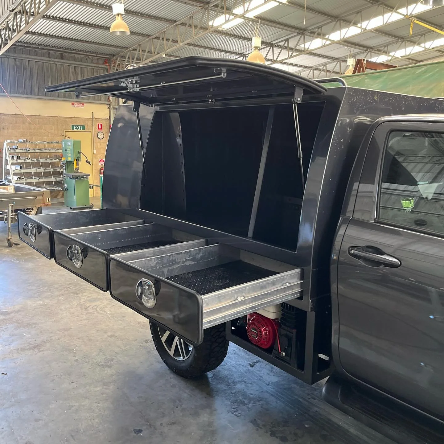 A black pickup truck with an open cargo storage and three metal drawers, located inside a warehouse or workshop.