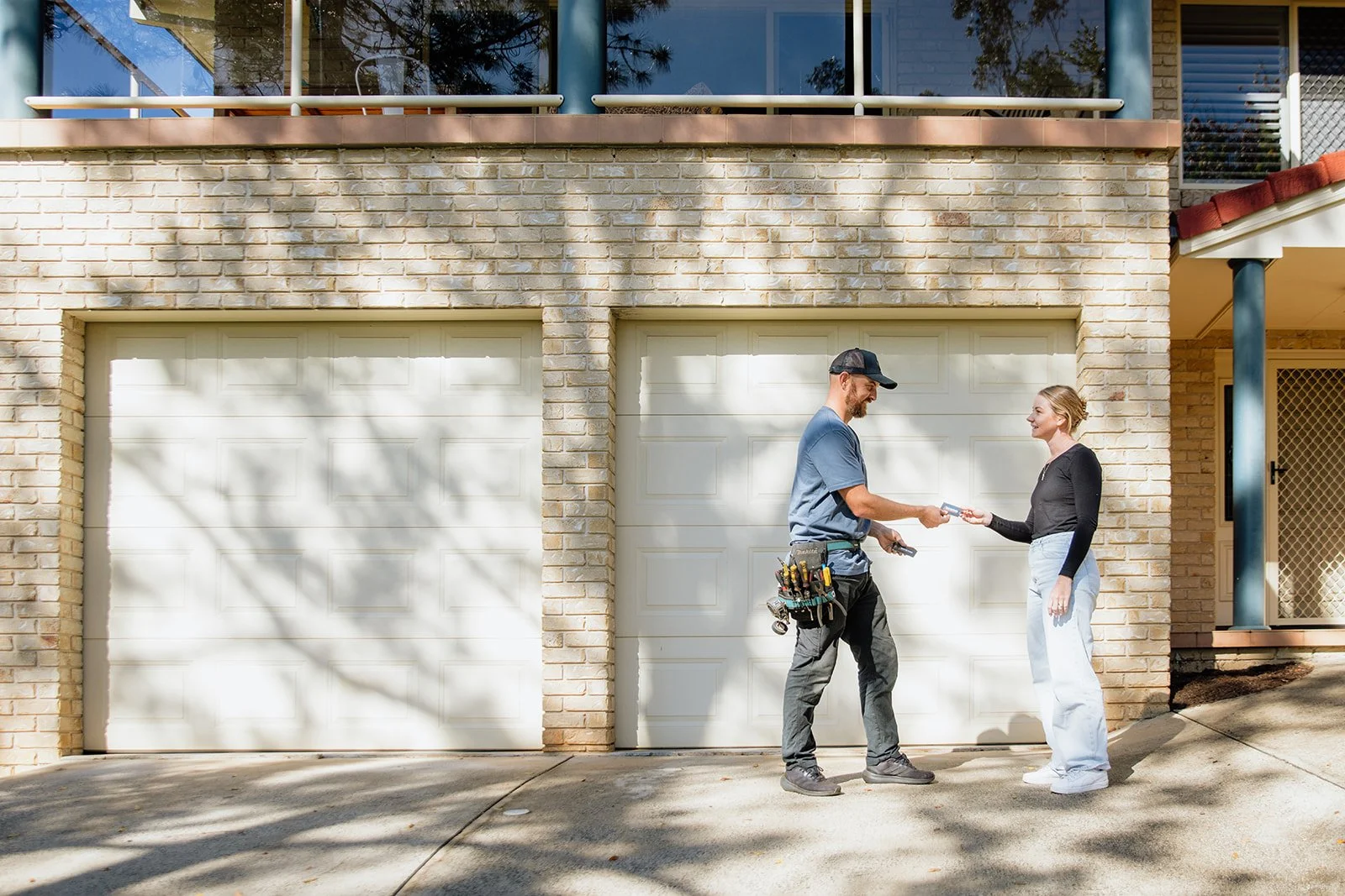 Ash from Back On Track Garage Doors hands his business card to a customer. There is a garage door behind them.