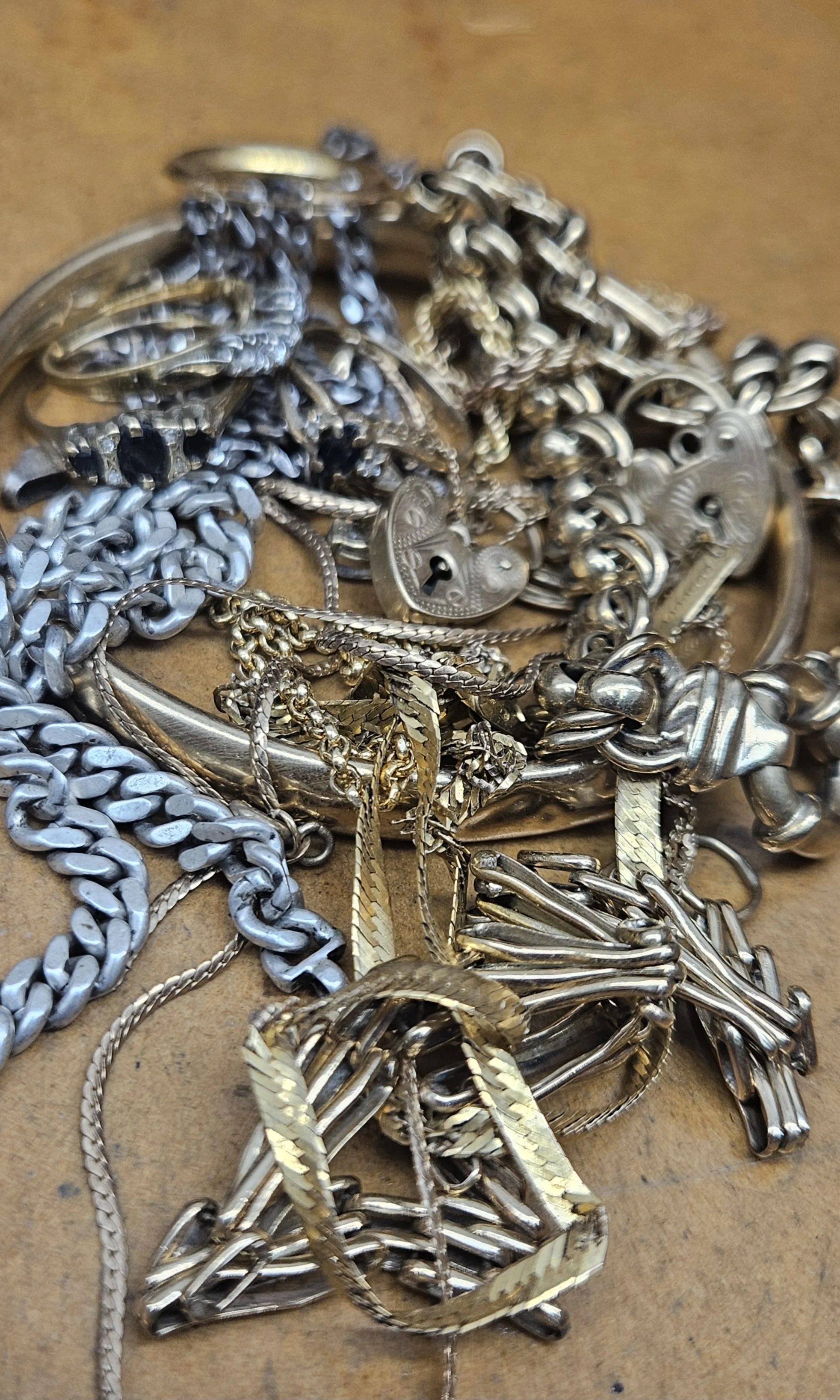 A pile of silver jewelry including chains, bracelets, and rings on a brown surface.