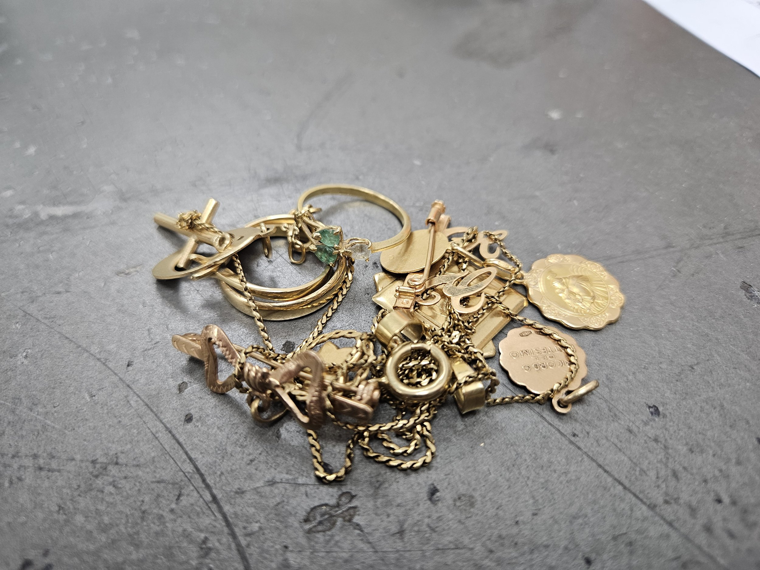 A pile of assorted gold-colored jewelry including rings, chains, and charms on a gray surface.