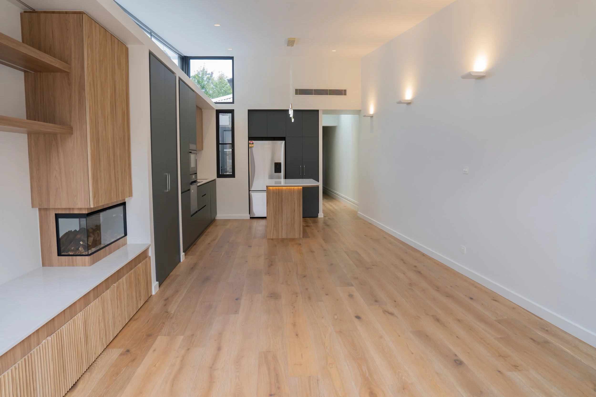 Modern kitchen with wooden flooring, gray cabinets, a white refrigerator, and natural light coming through large high windows.