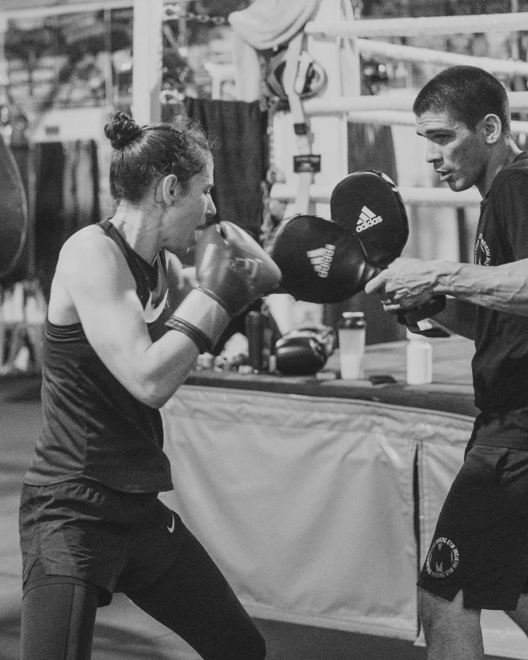 A female boxer practicing punches with a male trainer holding focus pads in a gym.