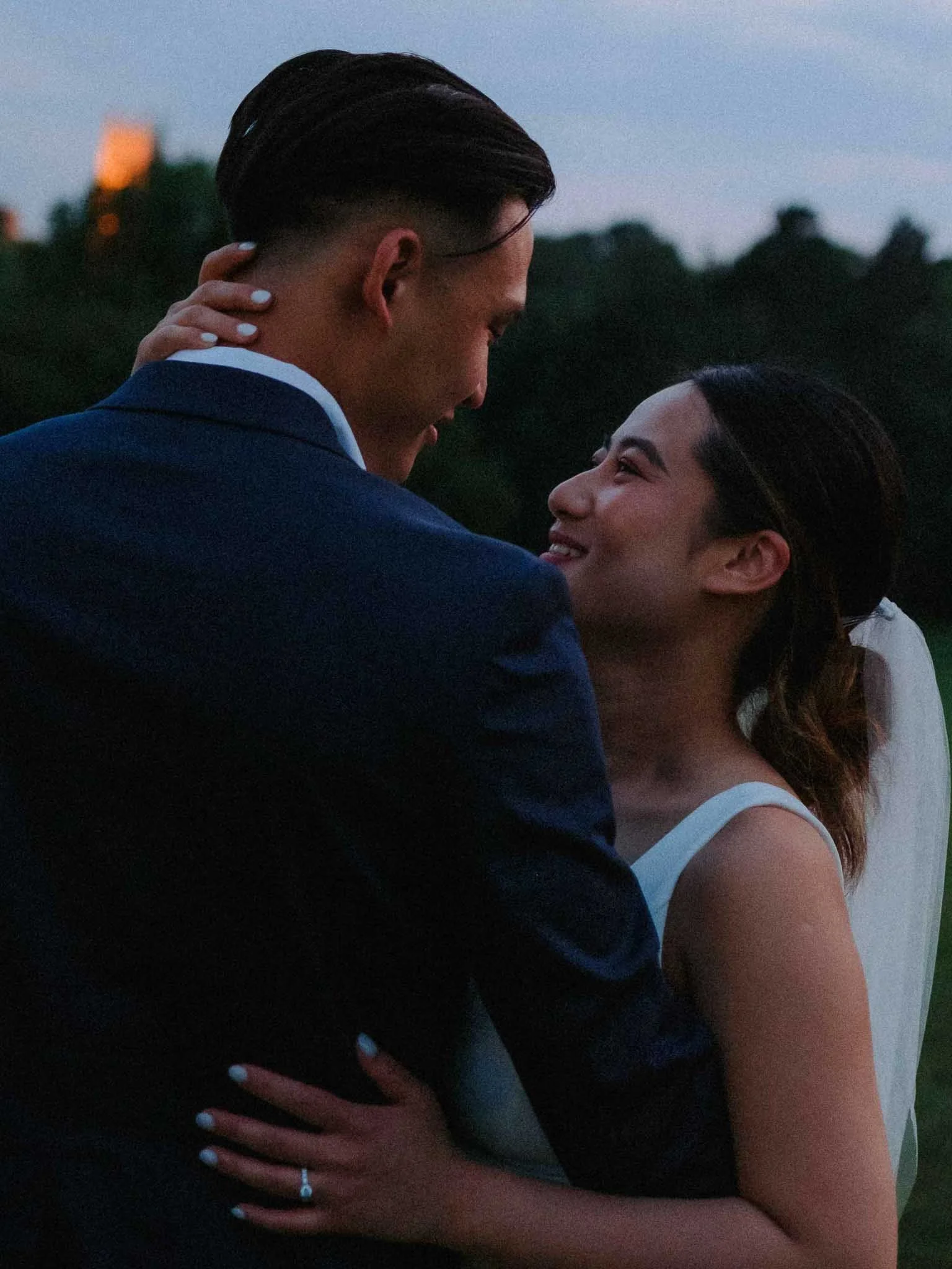 Bride and groom standing side by side, facing each other lovingly during a sunset photoshoot