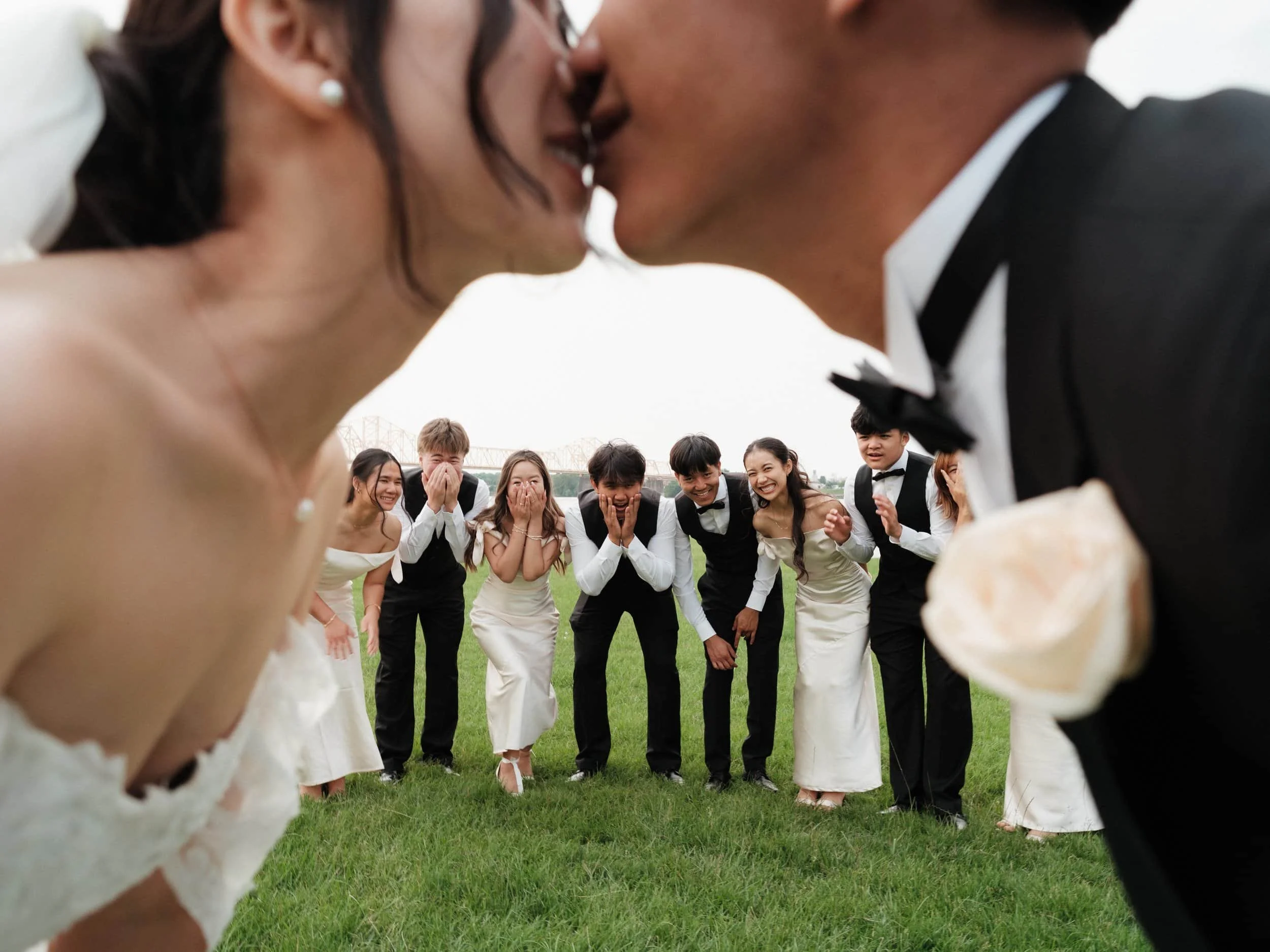 Out-of-focus photo of the bride and groom leaning in for a kiss while the wedding party looks on in awe in the background. North Carolina wedding photographer