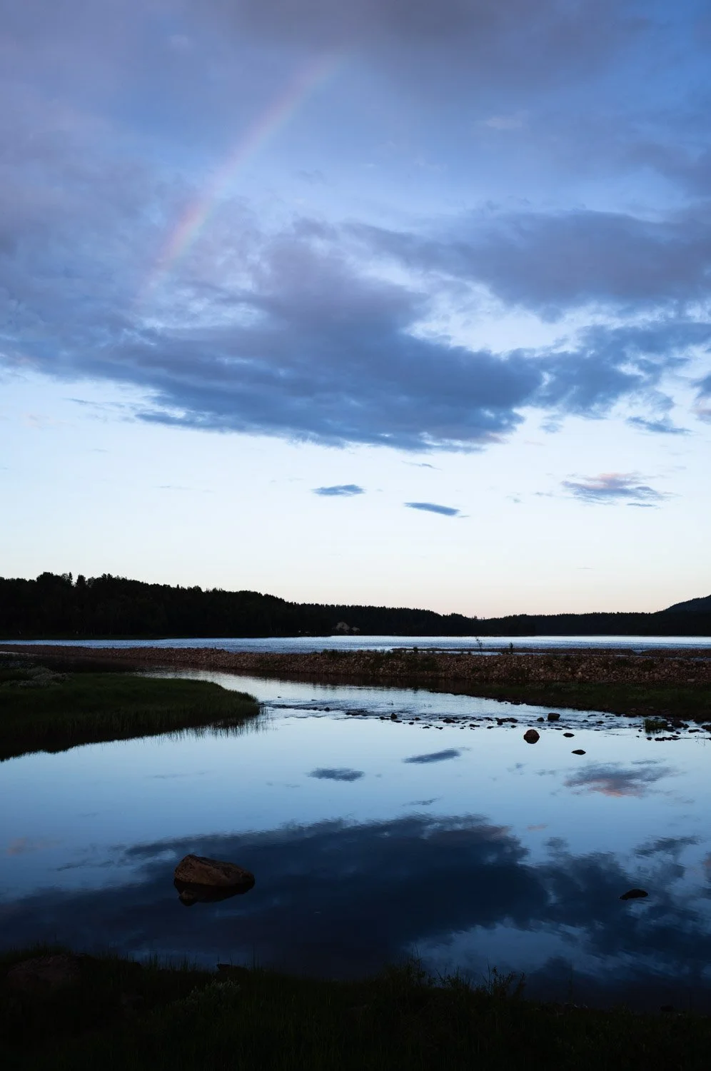 Regenbogen in der blauen Stunde über den ruhigen Gewässern des Storforsen