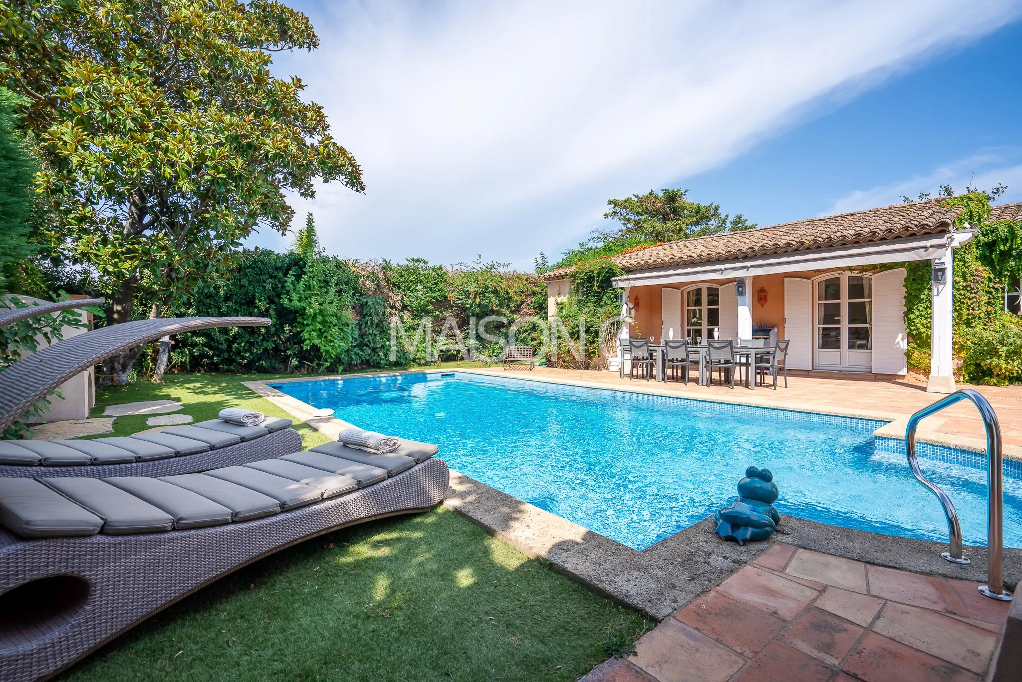 Piscine extérieure dans un jardin avec mobilier de détente et maison en arrière-plan