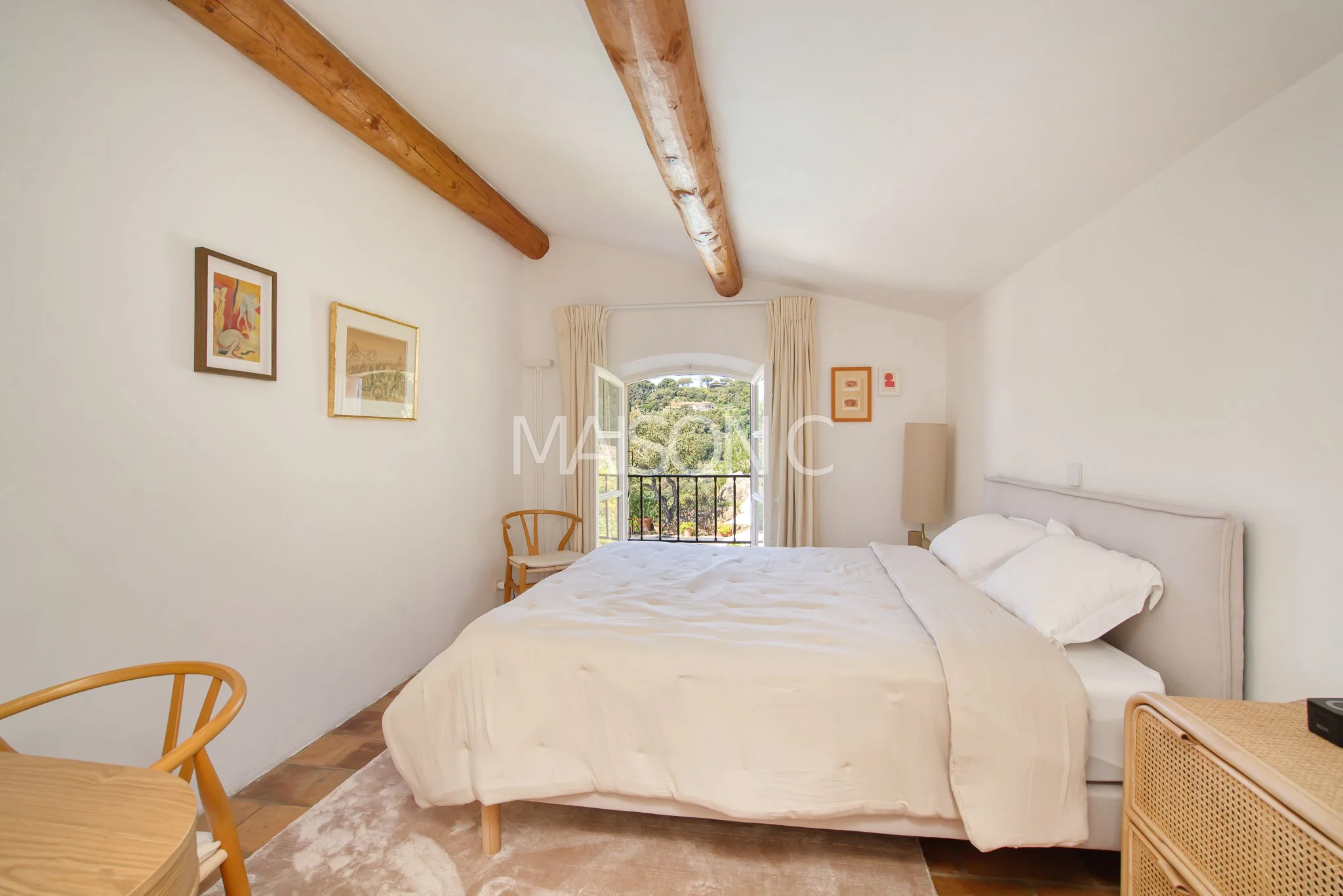 Chambre avec lit double blanc, lampadaire, quelques tableaux sur le mur, fenêtre avec vue sur la nature, meubles en bois naturel, tapis beige