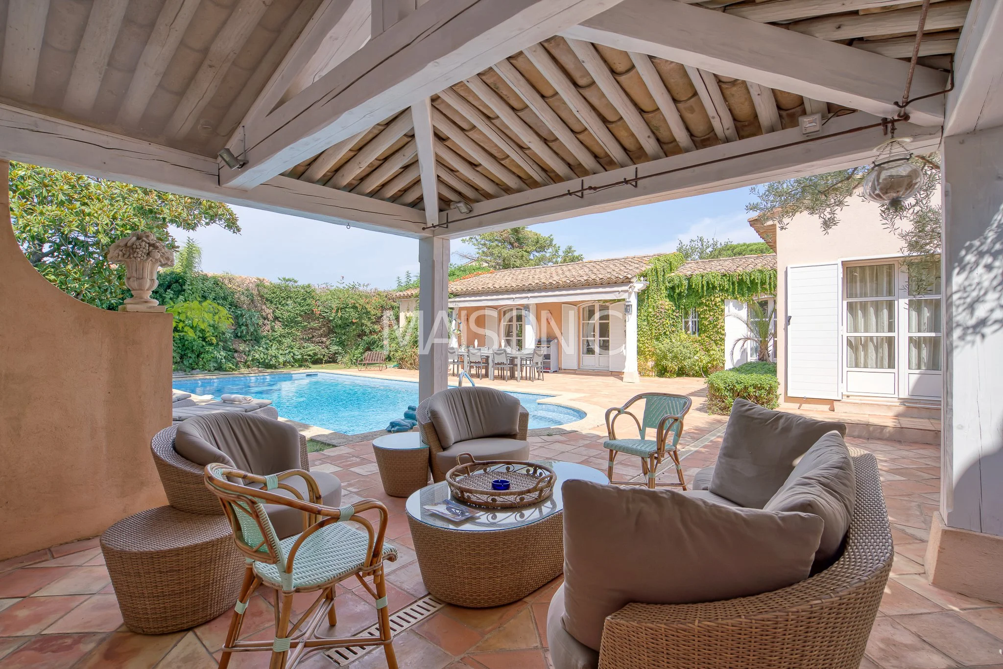 Espace extérieur avec piscine, coin salon avec fauteuils et table, jardin verdoyant dans une maison de style méditerranéen.