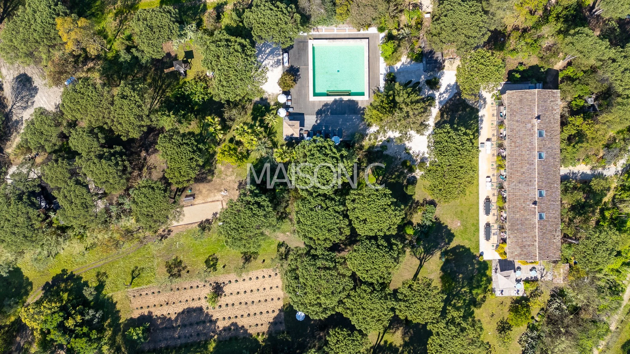 Vue aérienne d'une propriété avec une piscine, une maison rectangulaire avec de nombreux arbres et un espace verdoyant.