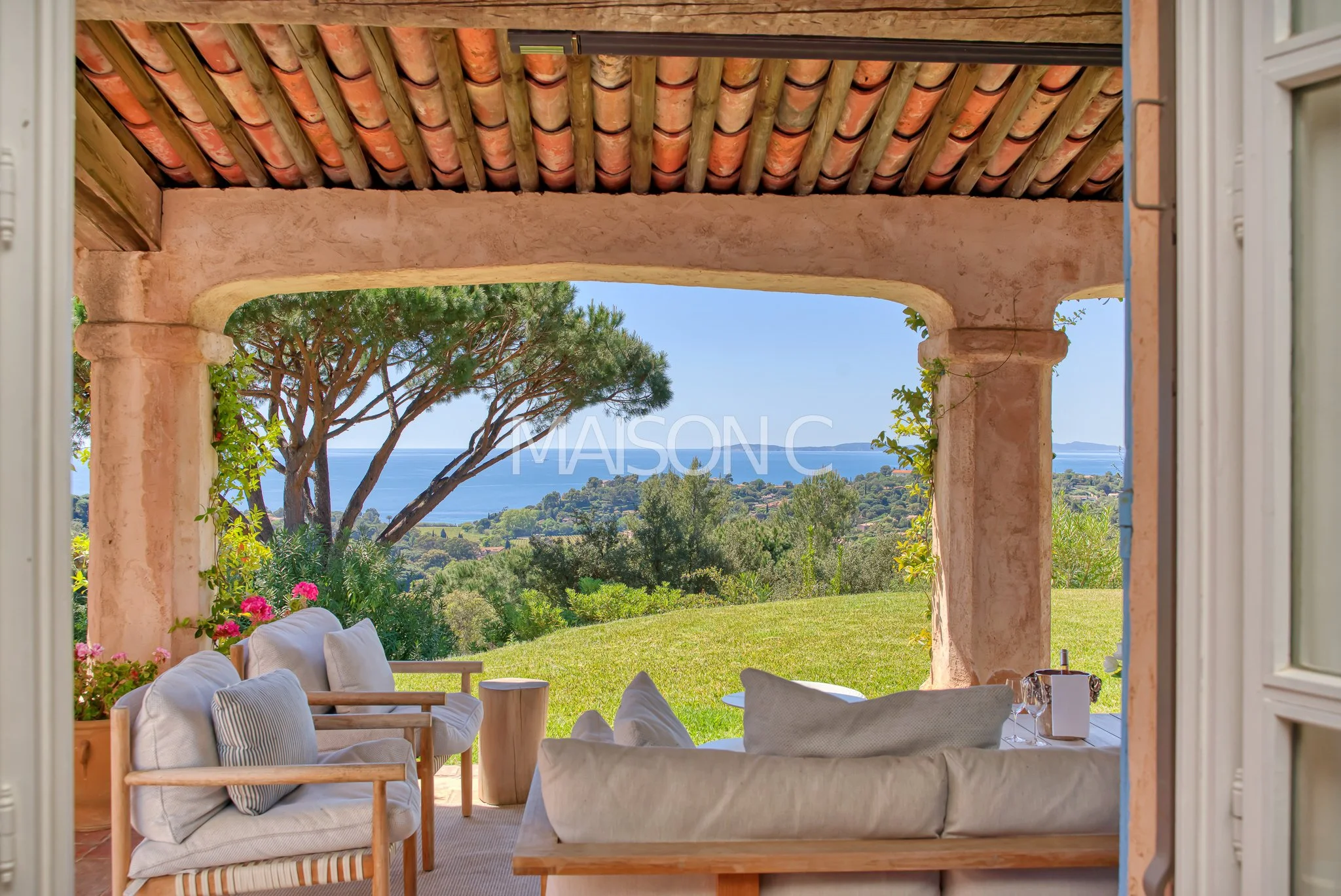 Terrasse avec mobilier en bois et coussins, vue sur la mer, arbres et terrain verdoyant