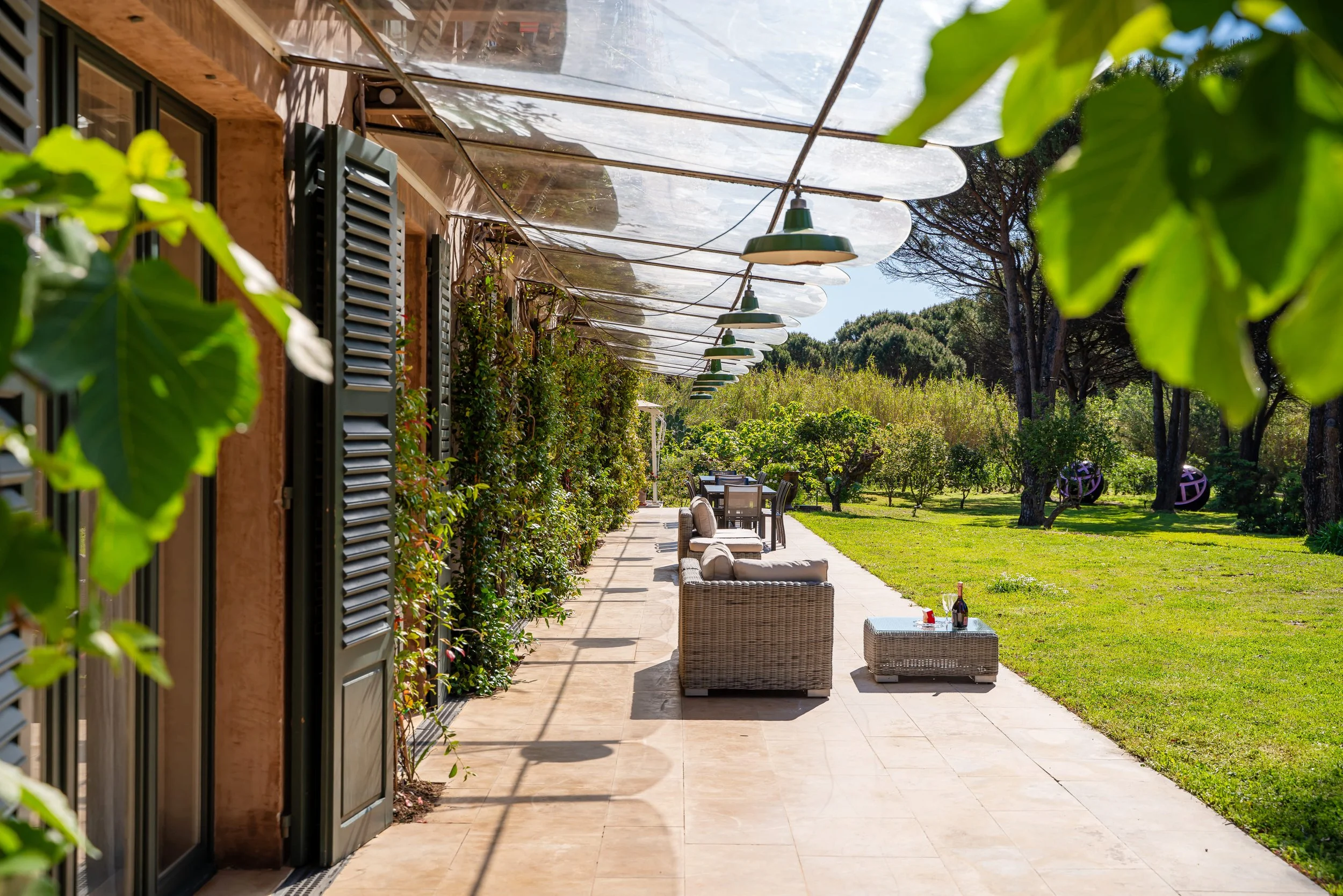 Porche d'une maison avec meubles en rotin et un espace de verdure avec des arbres et une pelouse