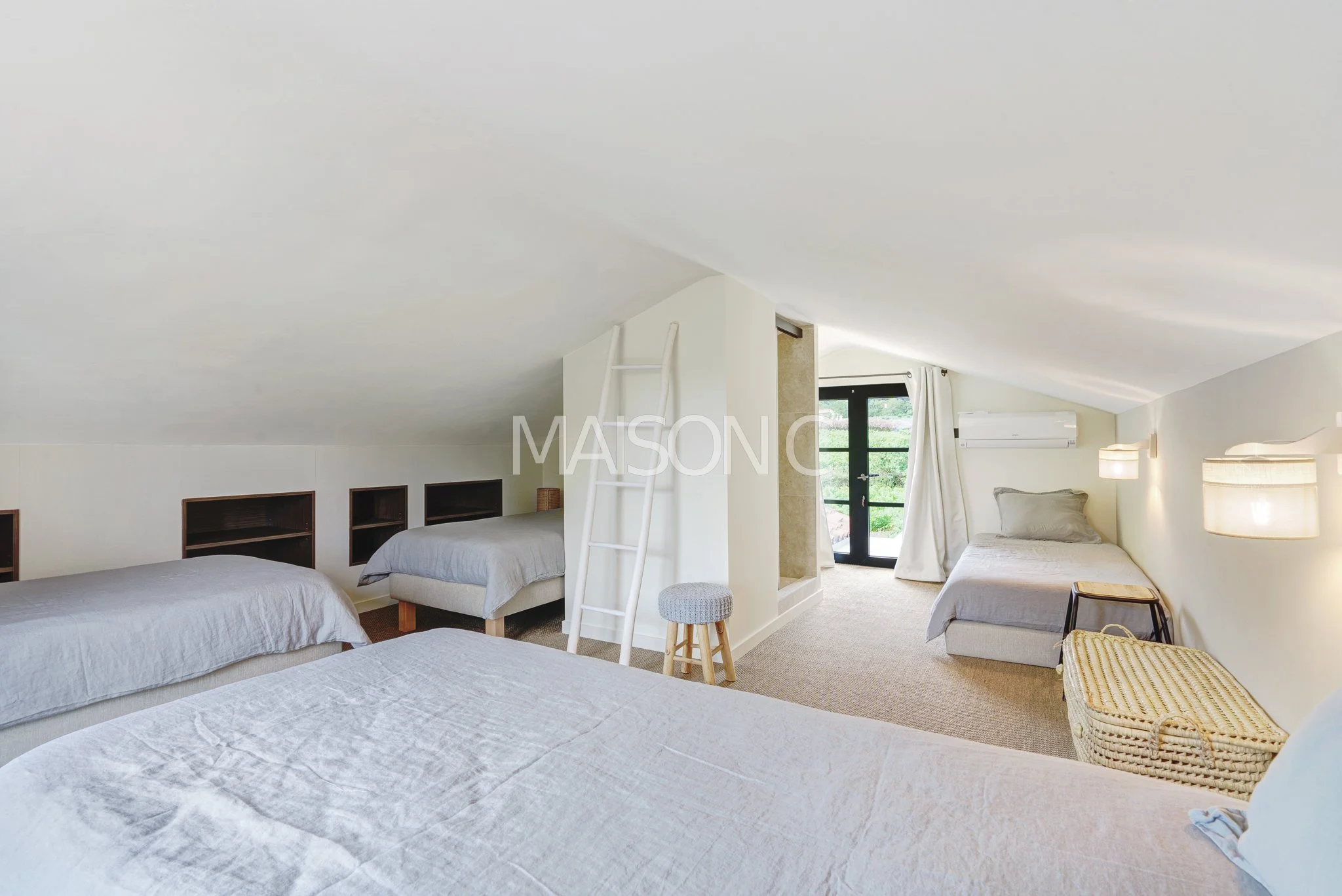 Chambre mansardée avec lit, lits simples, volet, porte-fenêtre donnant sur un balcon, fauteuil, panier, étagères intégrées